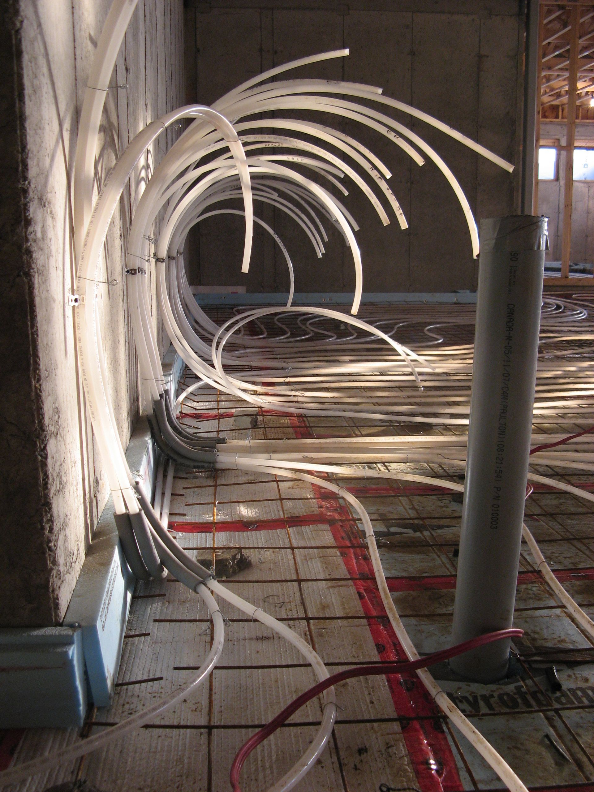 Pipes for radiant floor heating under construction, arranged in loops on a concrete floor near a wall.