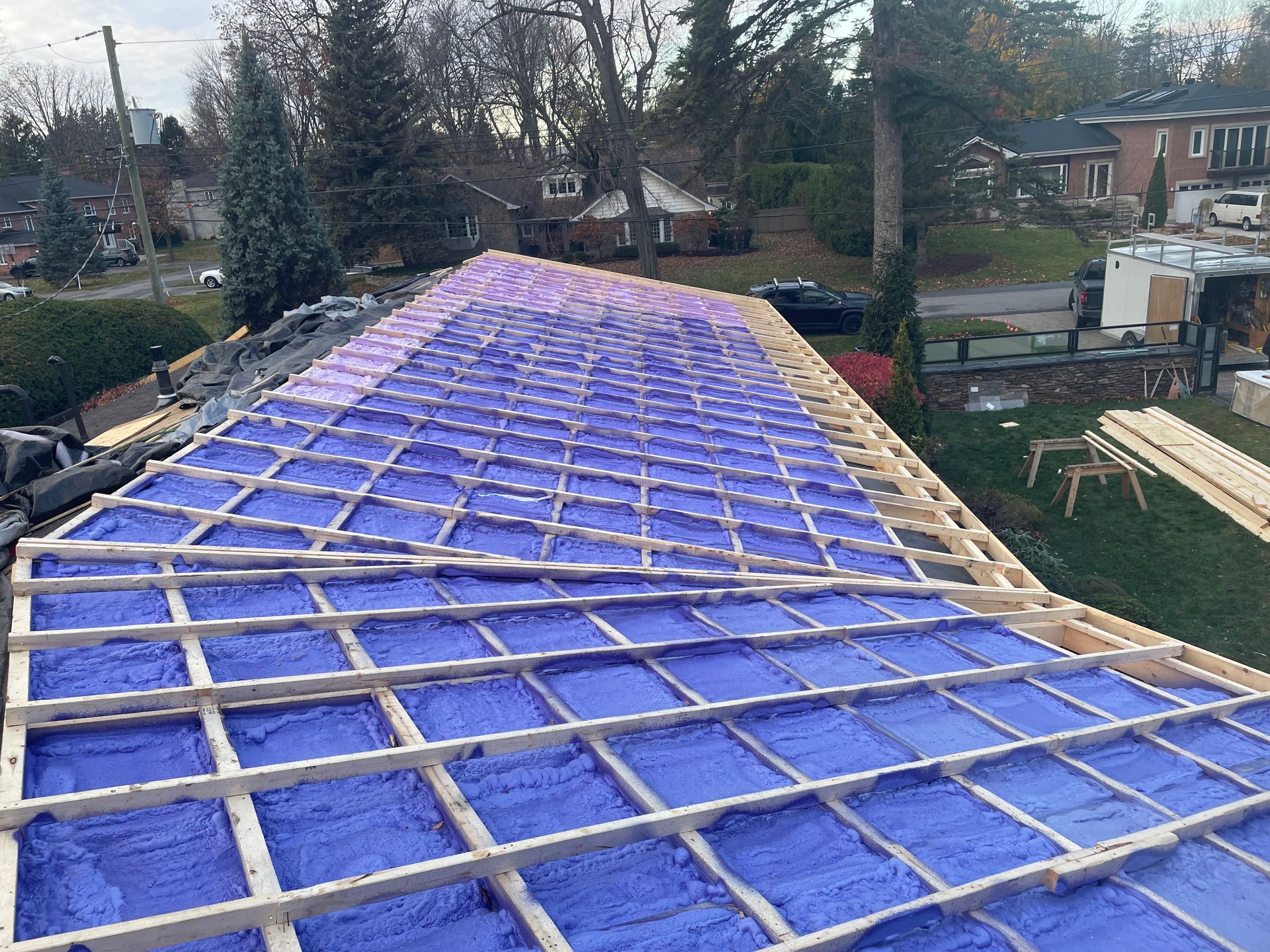 Roof under construction, purple insulation between wooden beams, partially completed.