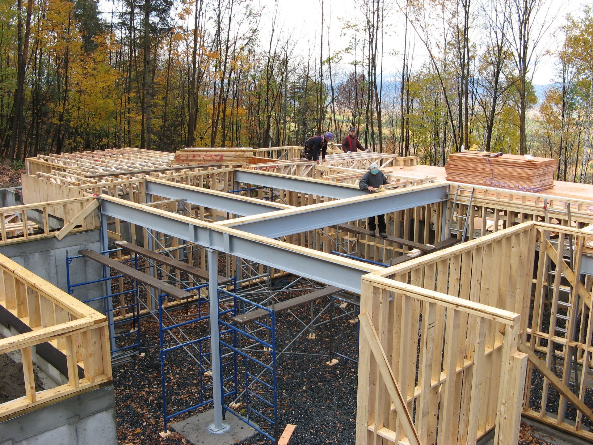 Construction of a wooden house frame with metal beams. Workers in background.