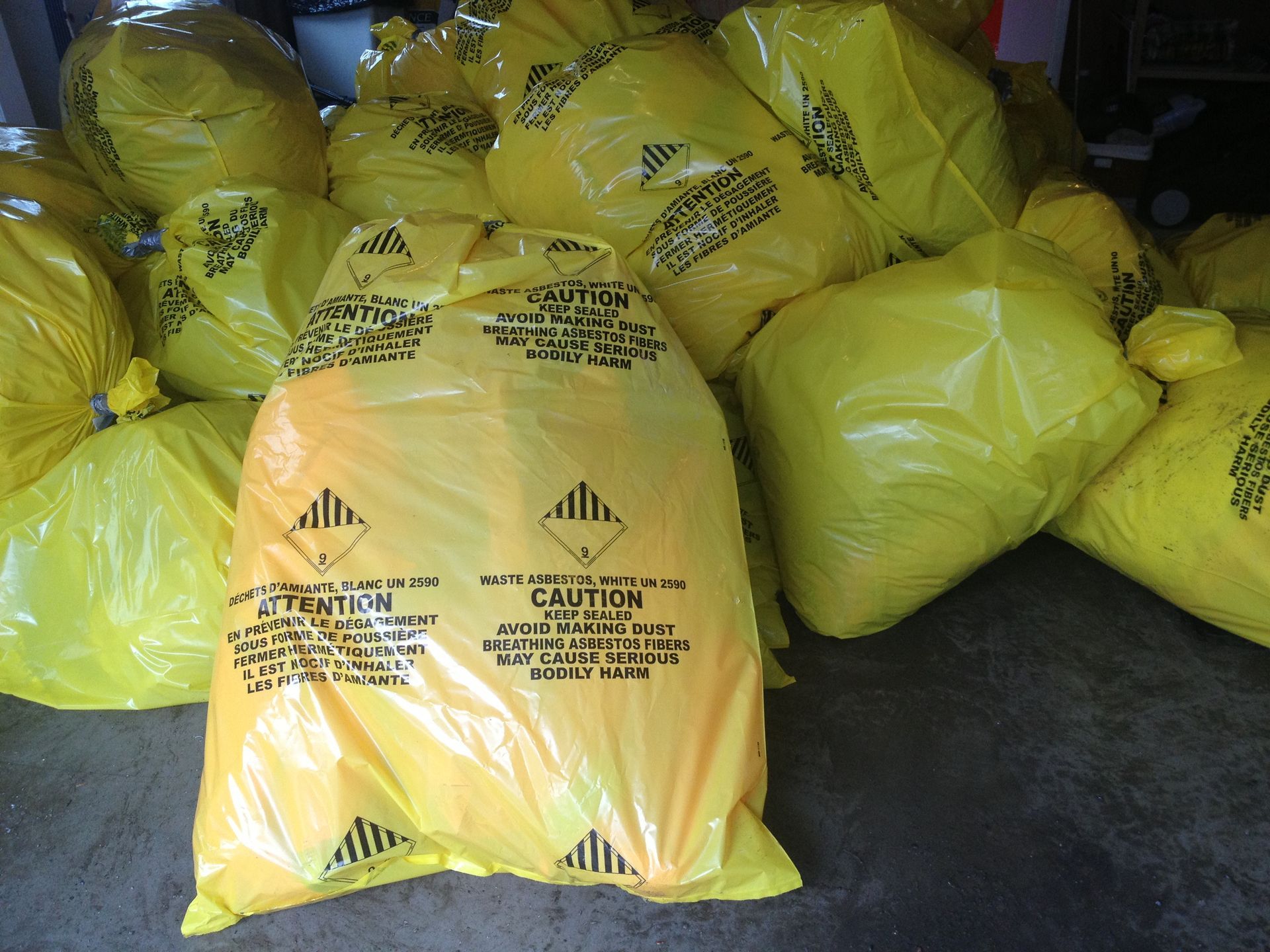 Yellow bags, potentially hazardous waste, are piled together. Warning symbols visible.