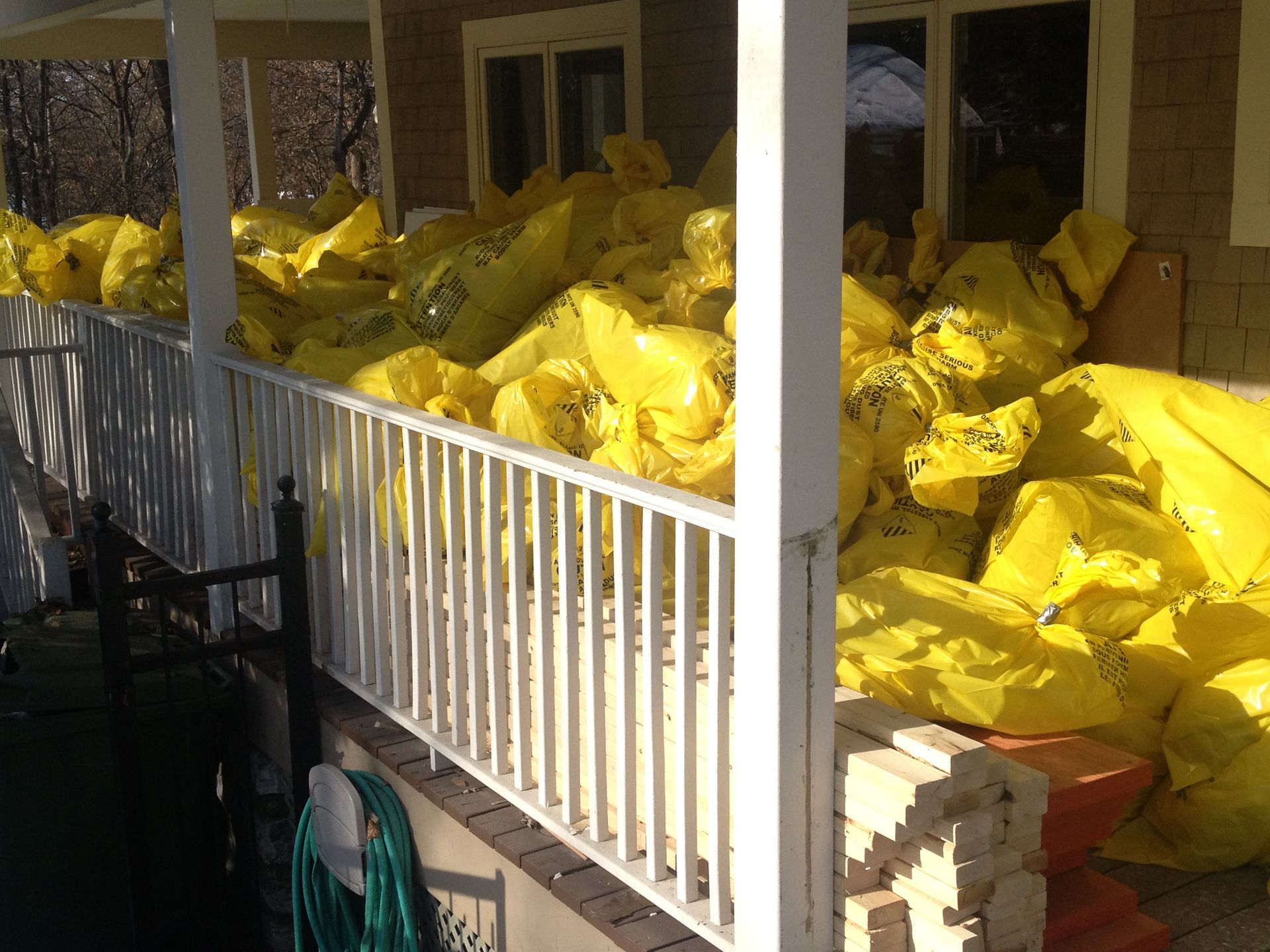 Yellow bags piled high on a porch, partially obscuring a railing and windows.