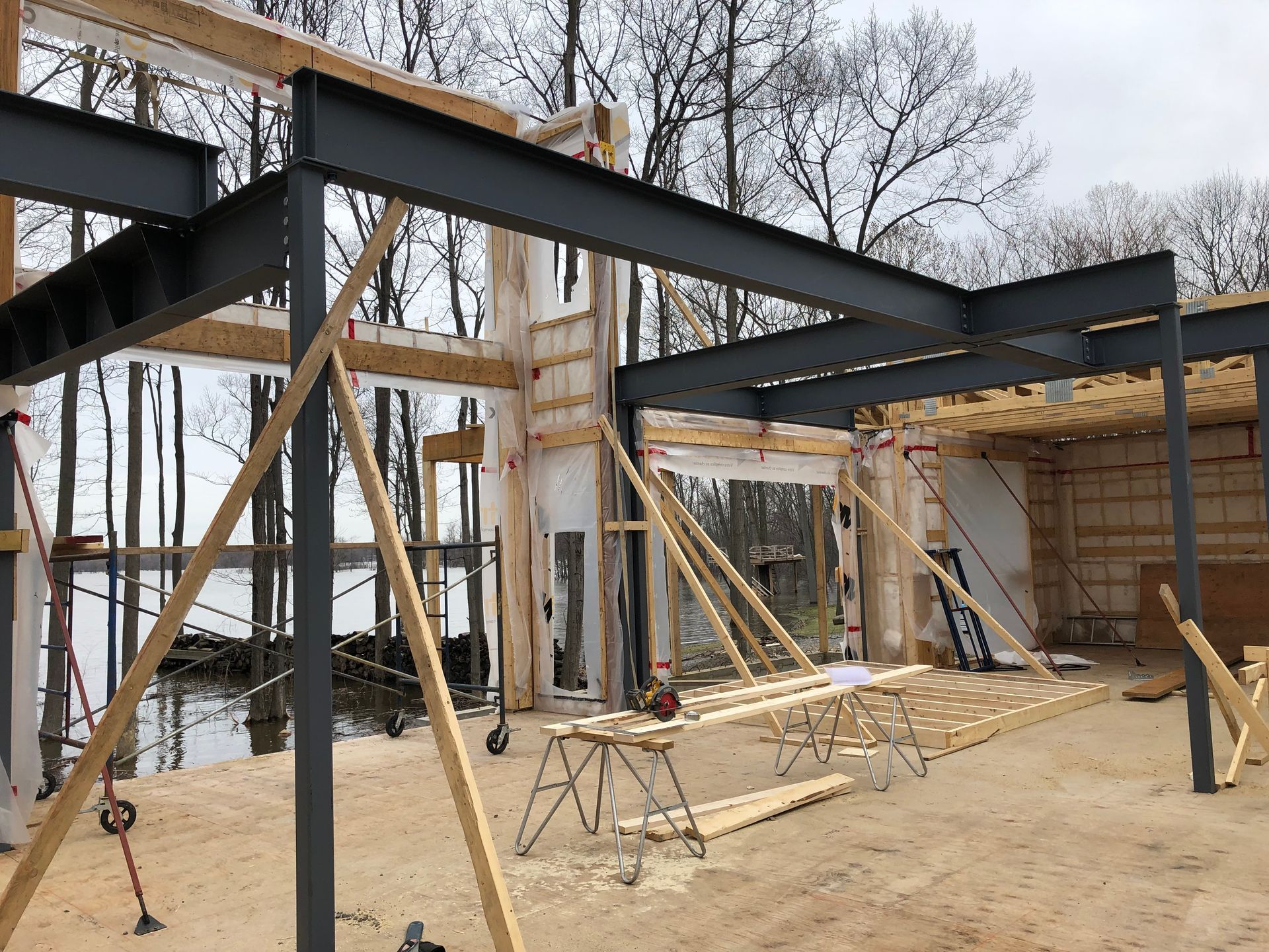 Construction site with exposed steel beams and wood framing, overlooking a body of water.