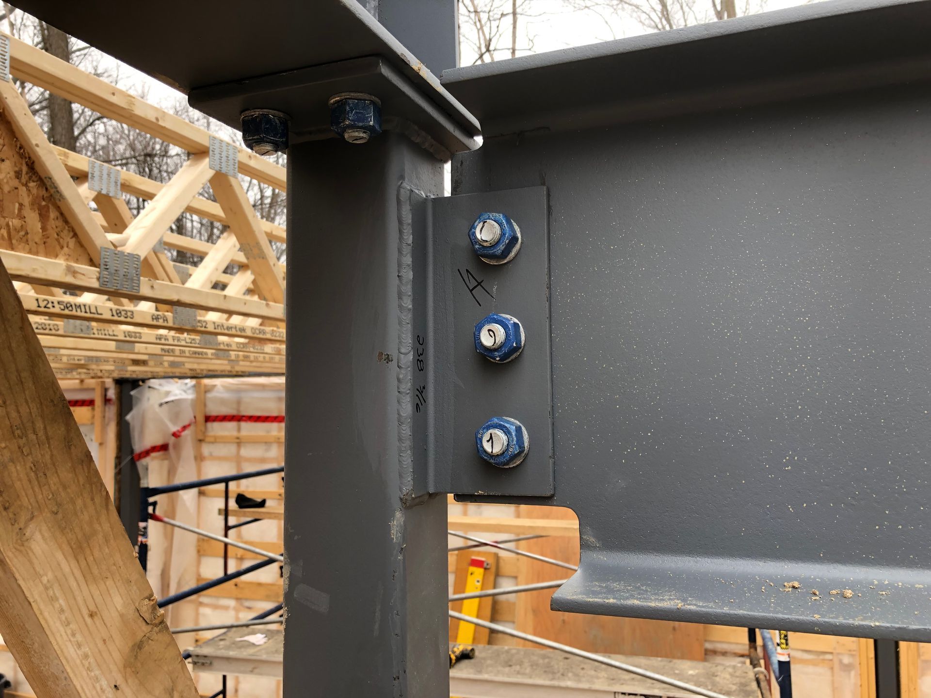 Steel beams bolted together, part of a building frame. Gray beams, blue bolts. Construction site.