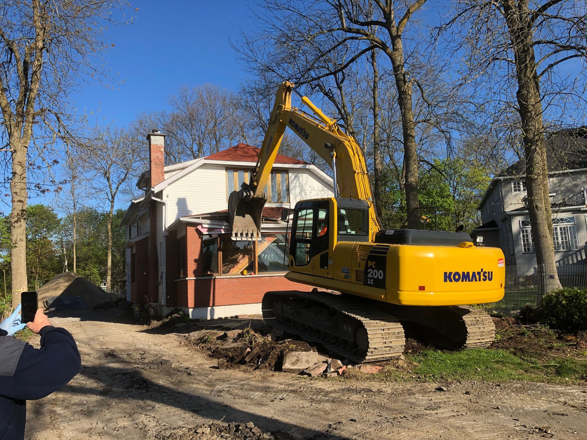 Yellow Komatsu excavator demolishing a brick and stucco building with a red tile roof.