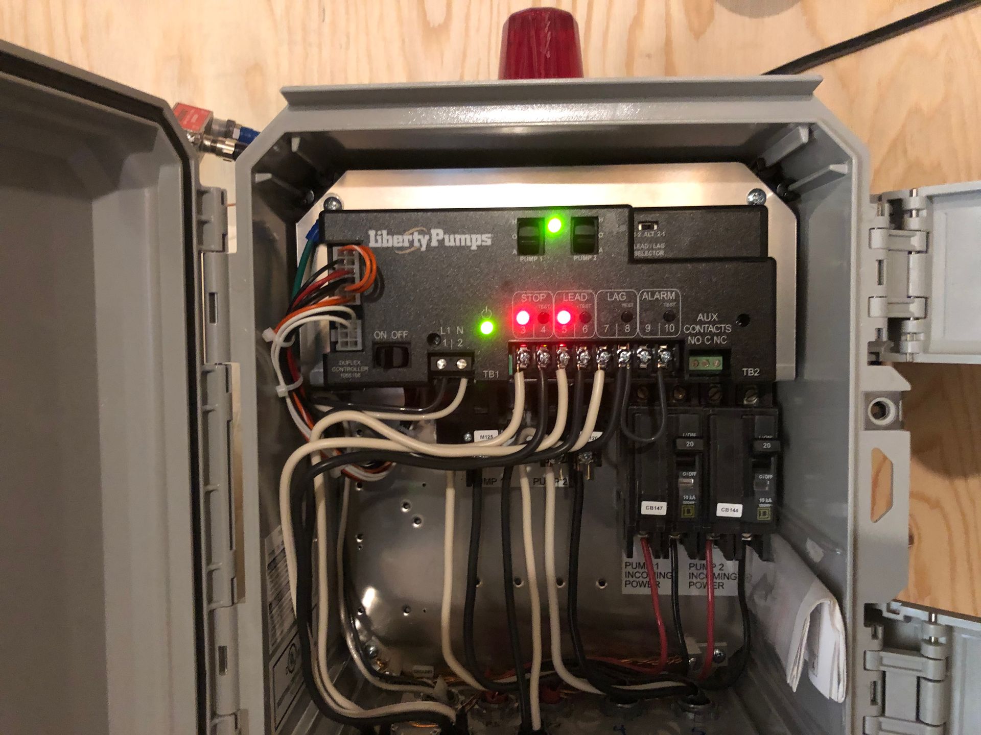Grey electrical control box, Liberty Pumps brand, with lights, wires, and switches mounted on a wall.