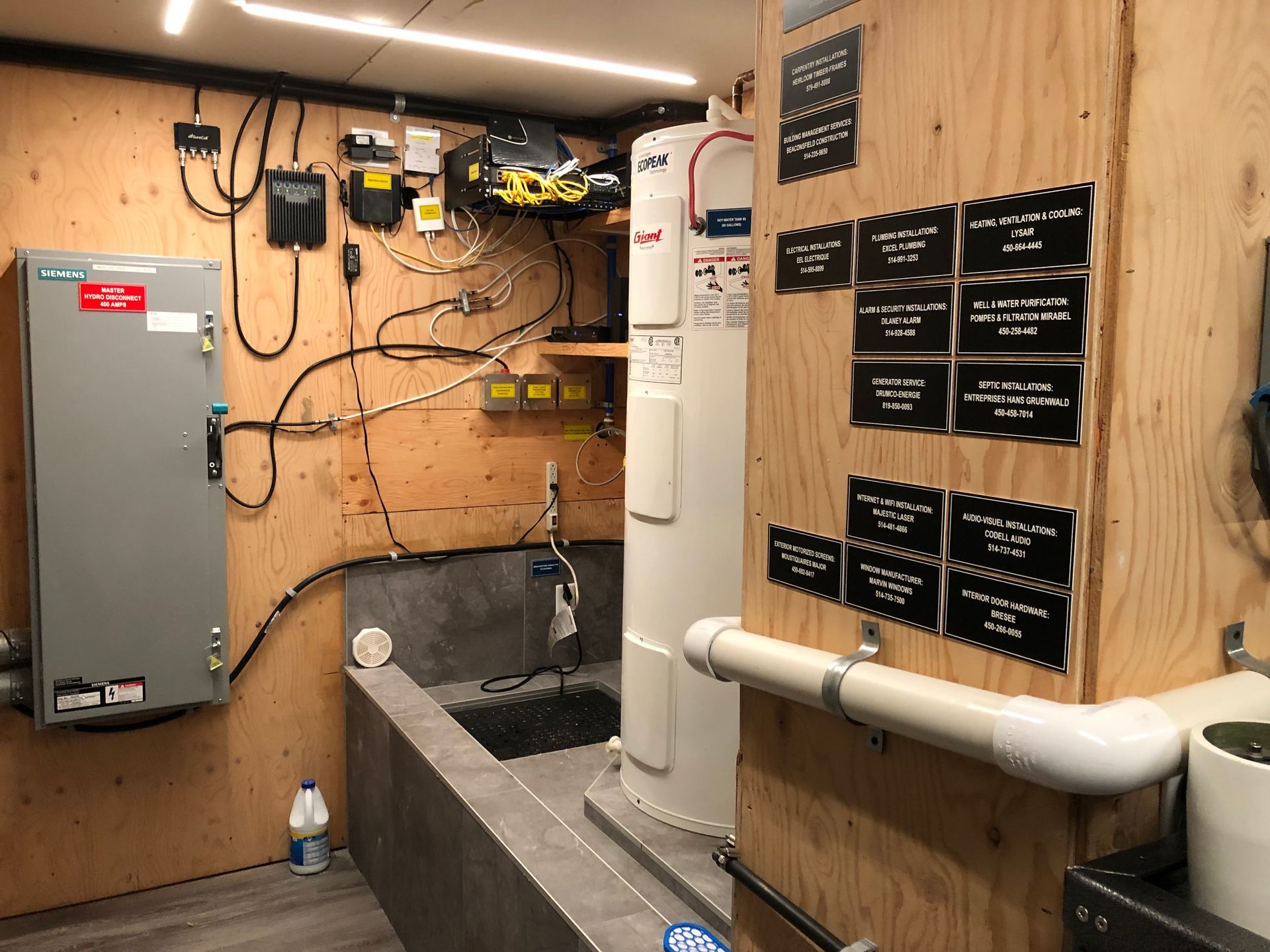 Indoor utility room with electrical equipment, water heater, and notes on a wooden wall.