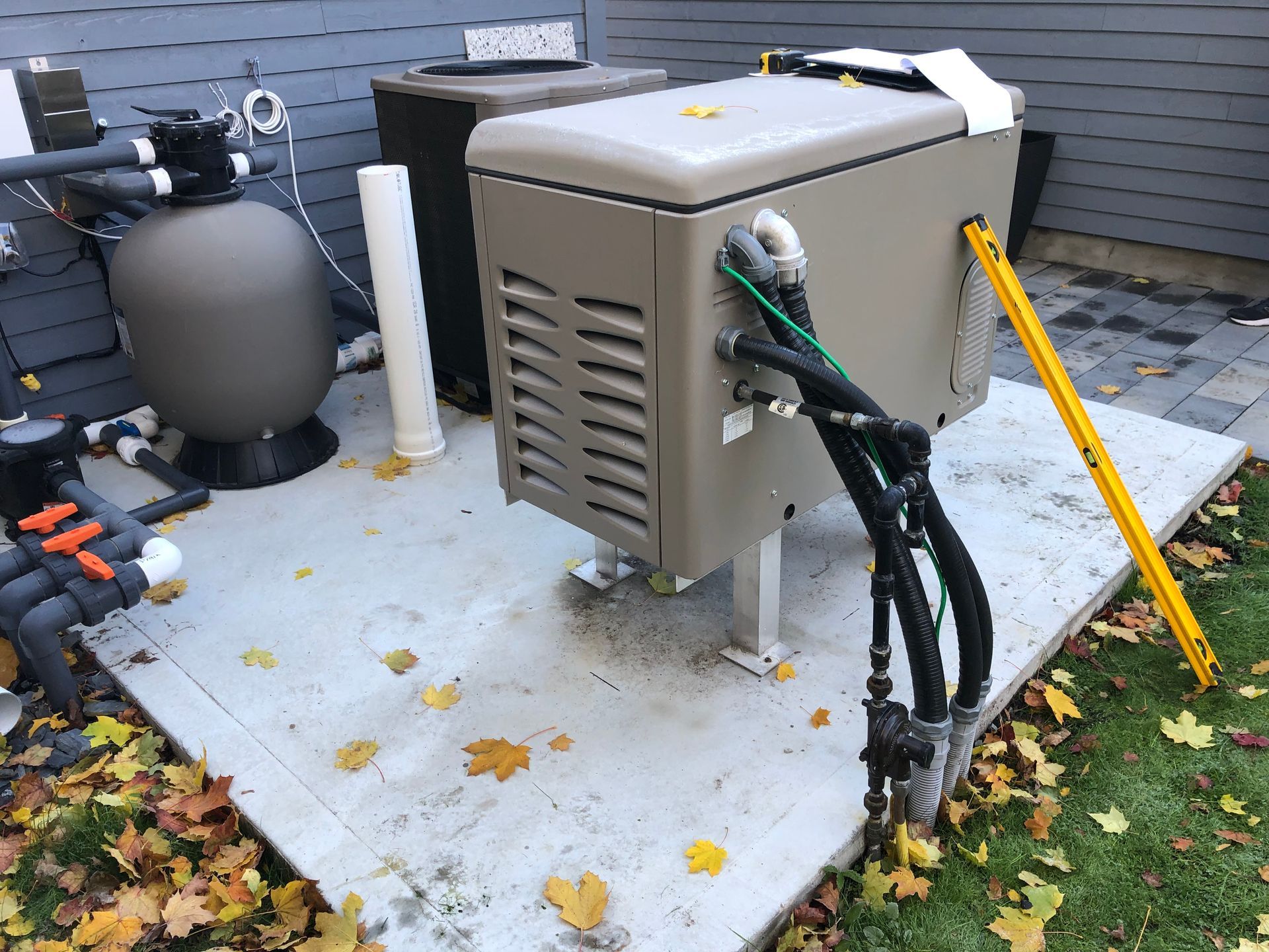 Pool equipment on a concrete pad with fallen leaves; includes a heater, filter, and plumbing.