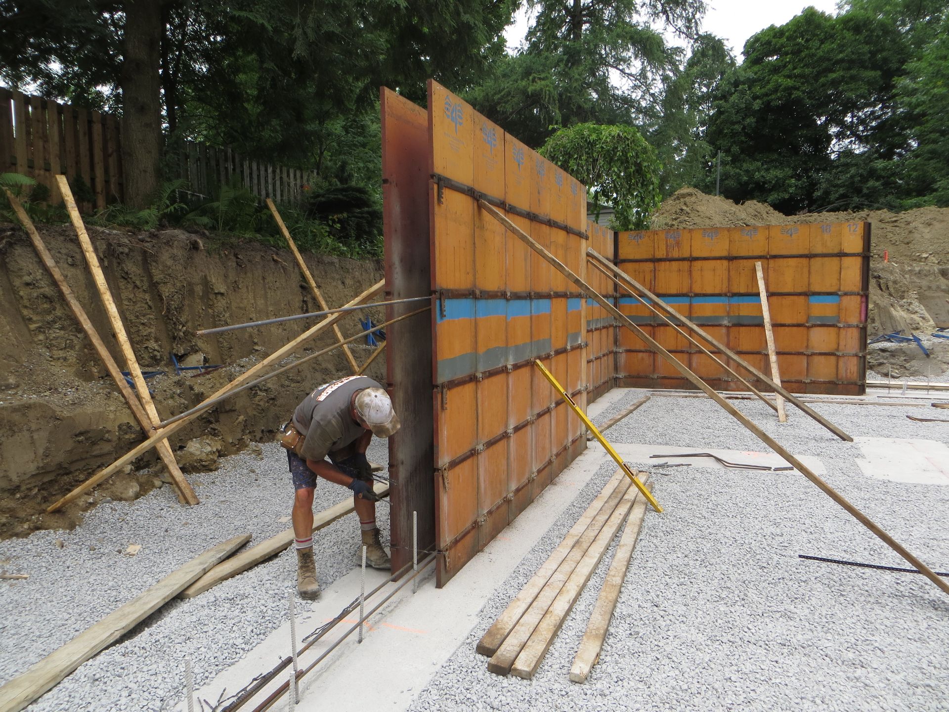 Construction worker with concrete forms in a gravel foundation, bracing walls.