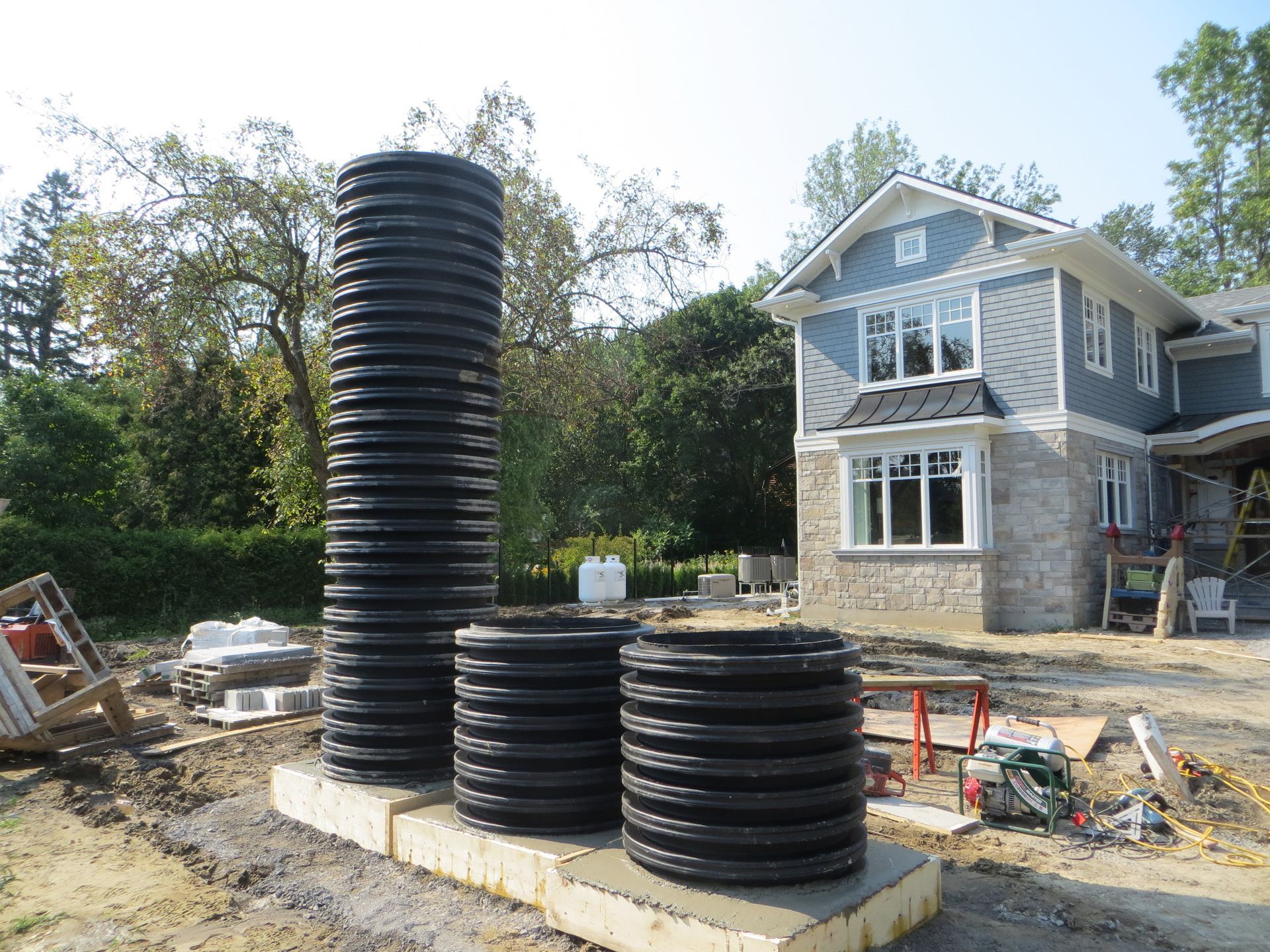 Black corrugated plastic tanks on a concrete base, near a house under construction.