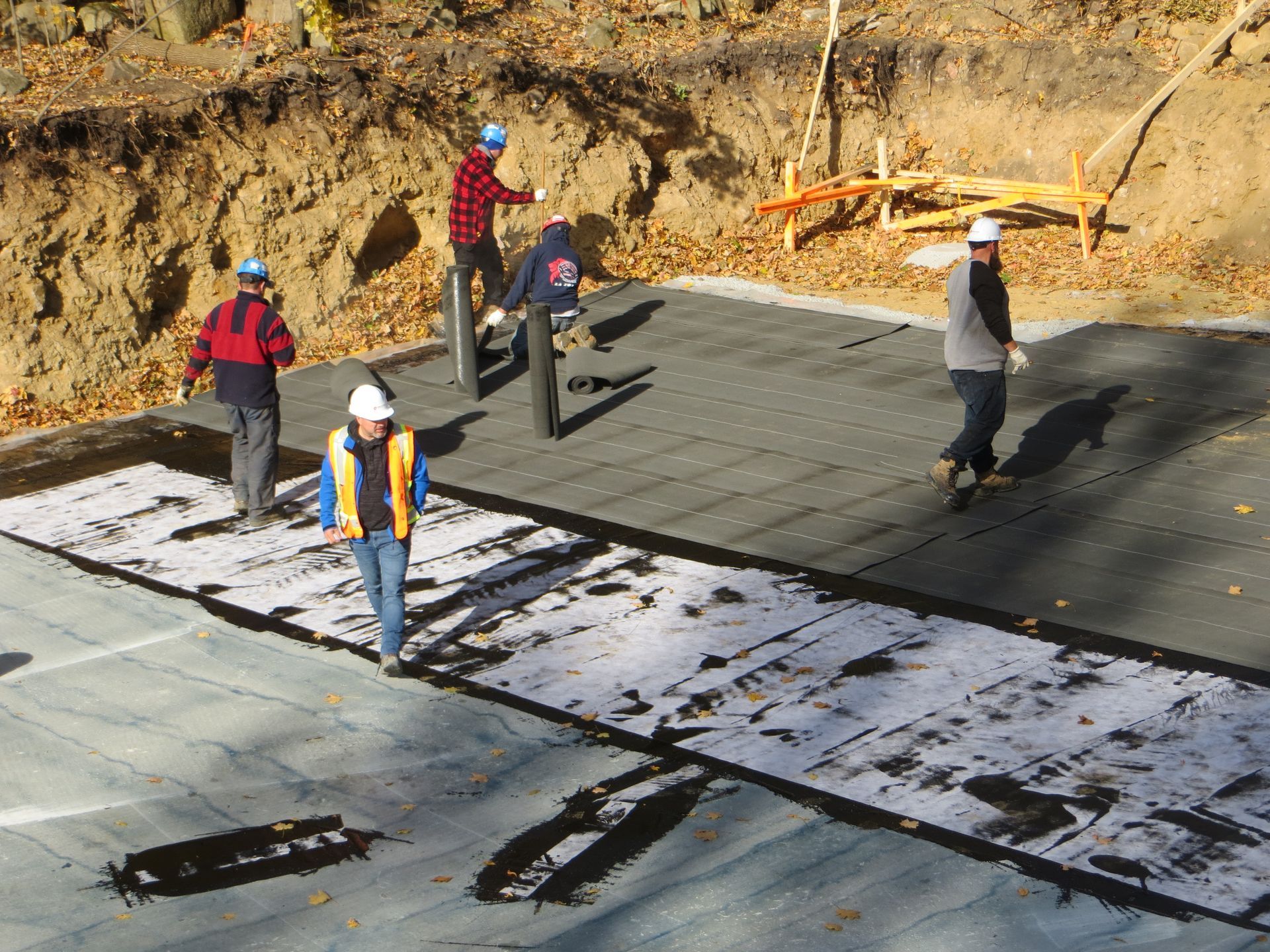 Construction workers on a paved surface, preparing for a project outdoors, near a dirt embankment.