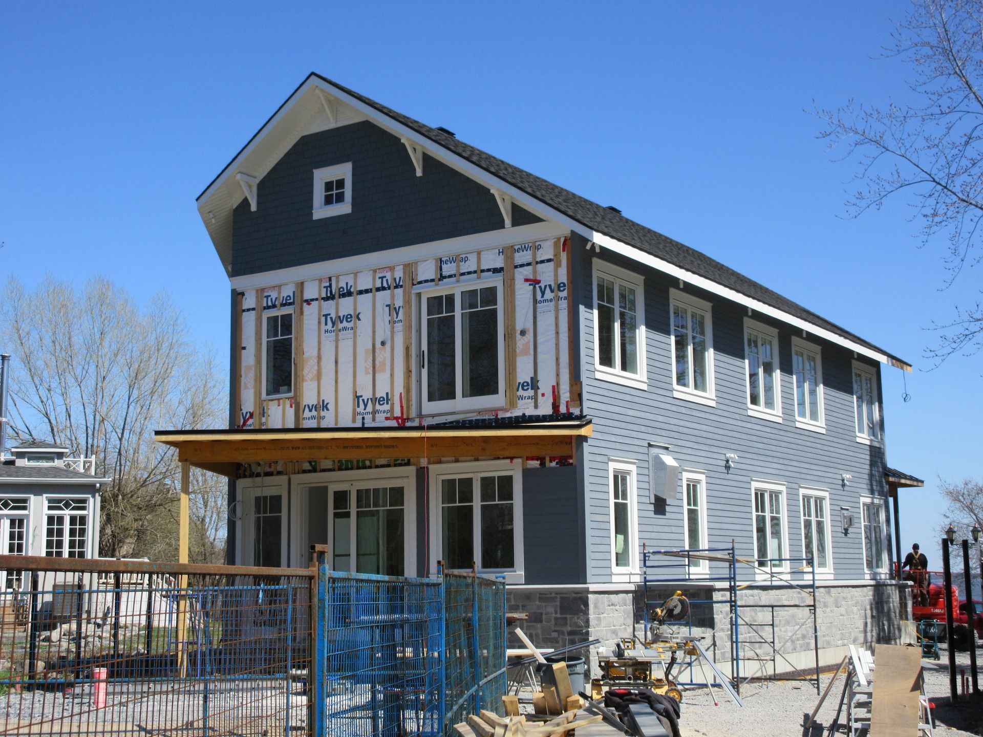 Two-story house under construction, blue siding, white trim, with a porch and construction materials visible.
