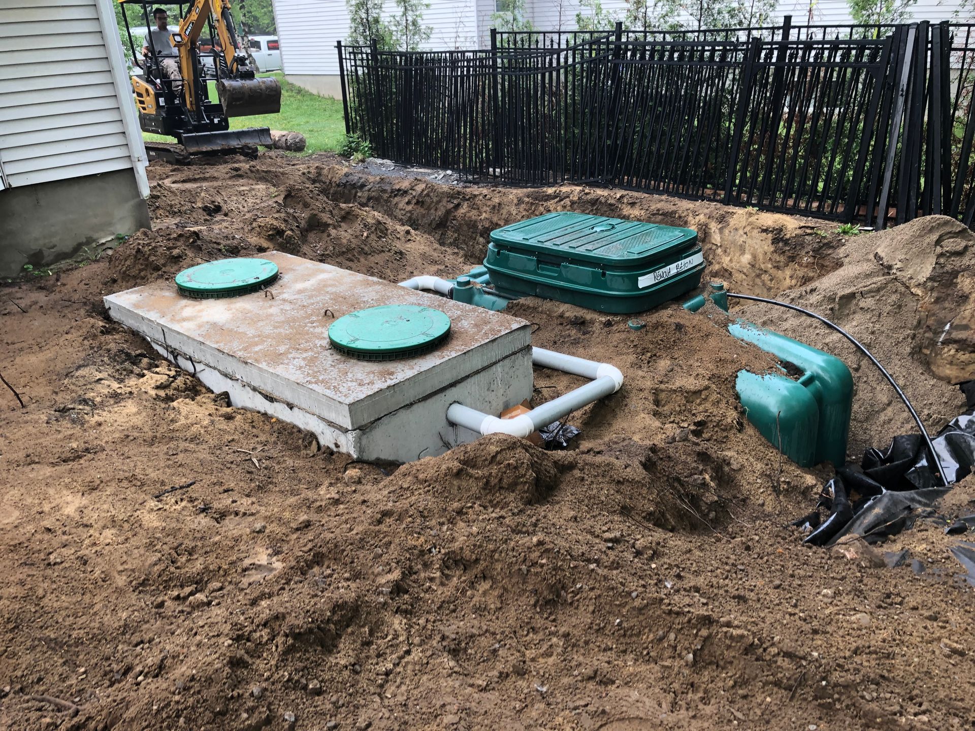 Septic system installation: concrete tank, green lids, connecting pipes, and a smaller control box in a dirt trench.