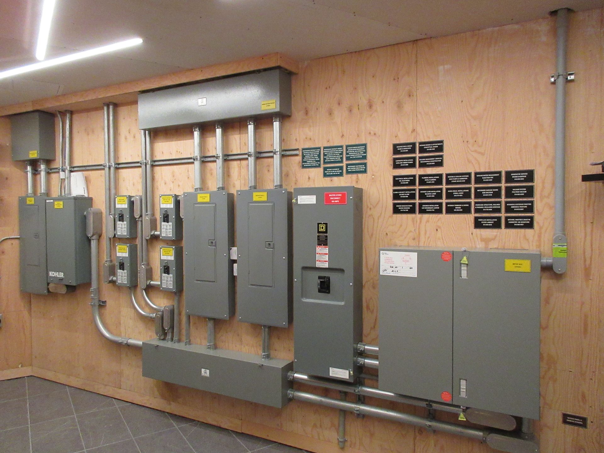 Electrical equipment installed on a wooden wall, including gray electrical panels, boxes, and conduit.