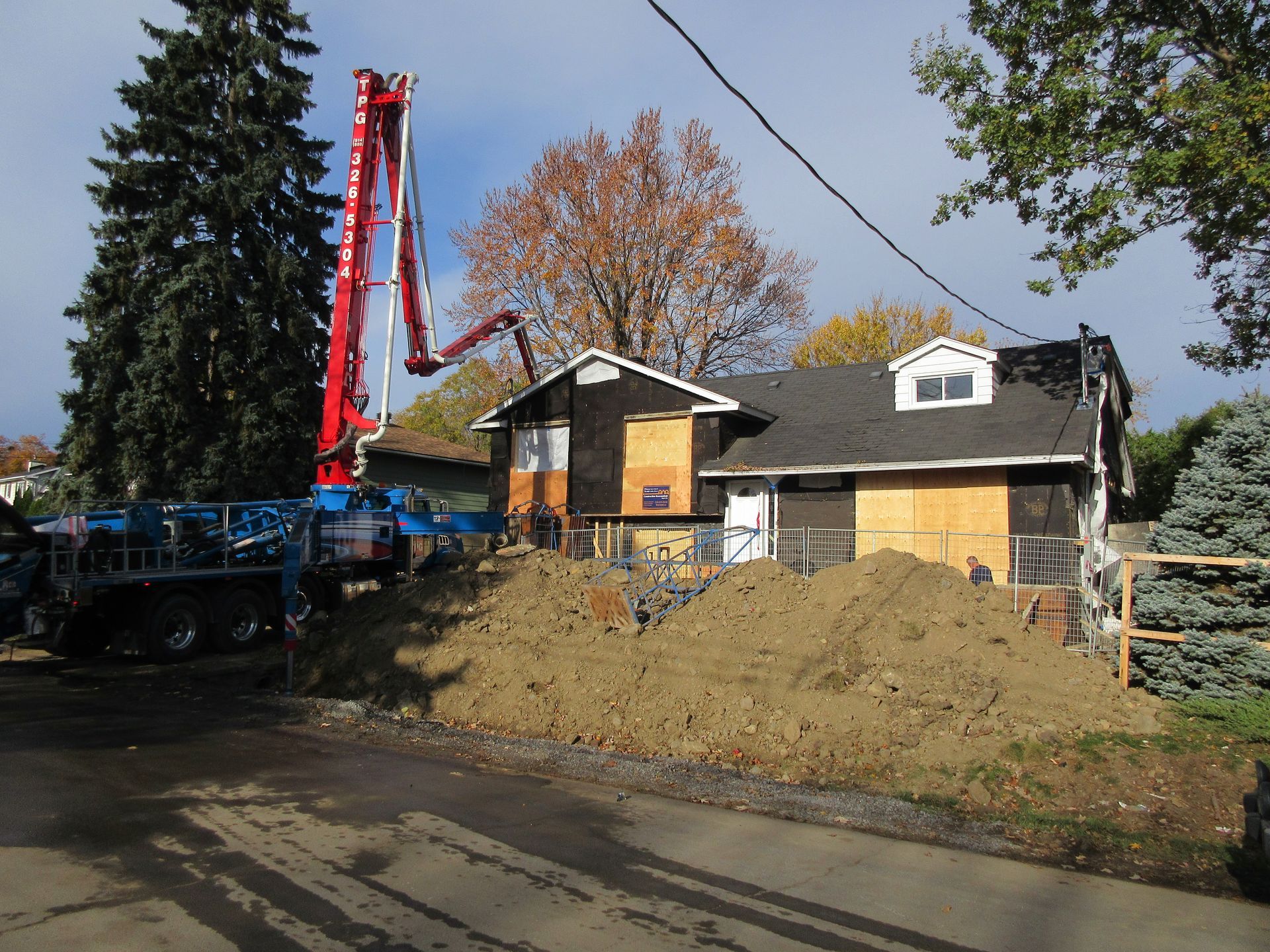 Concrete pump truck pouring concrete at a house under construction; dirt mound in front.