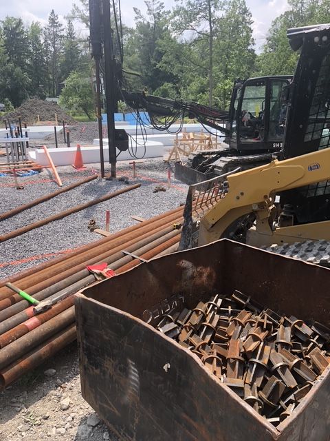 Construction site with excavator and metal beams, pipes, and bucket.