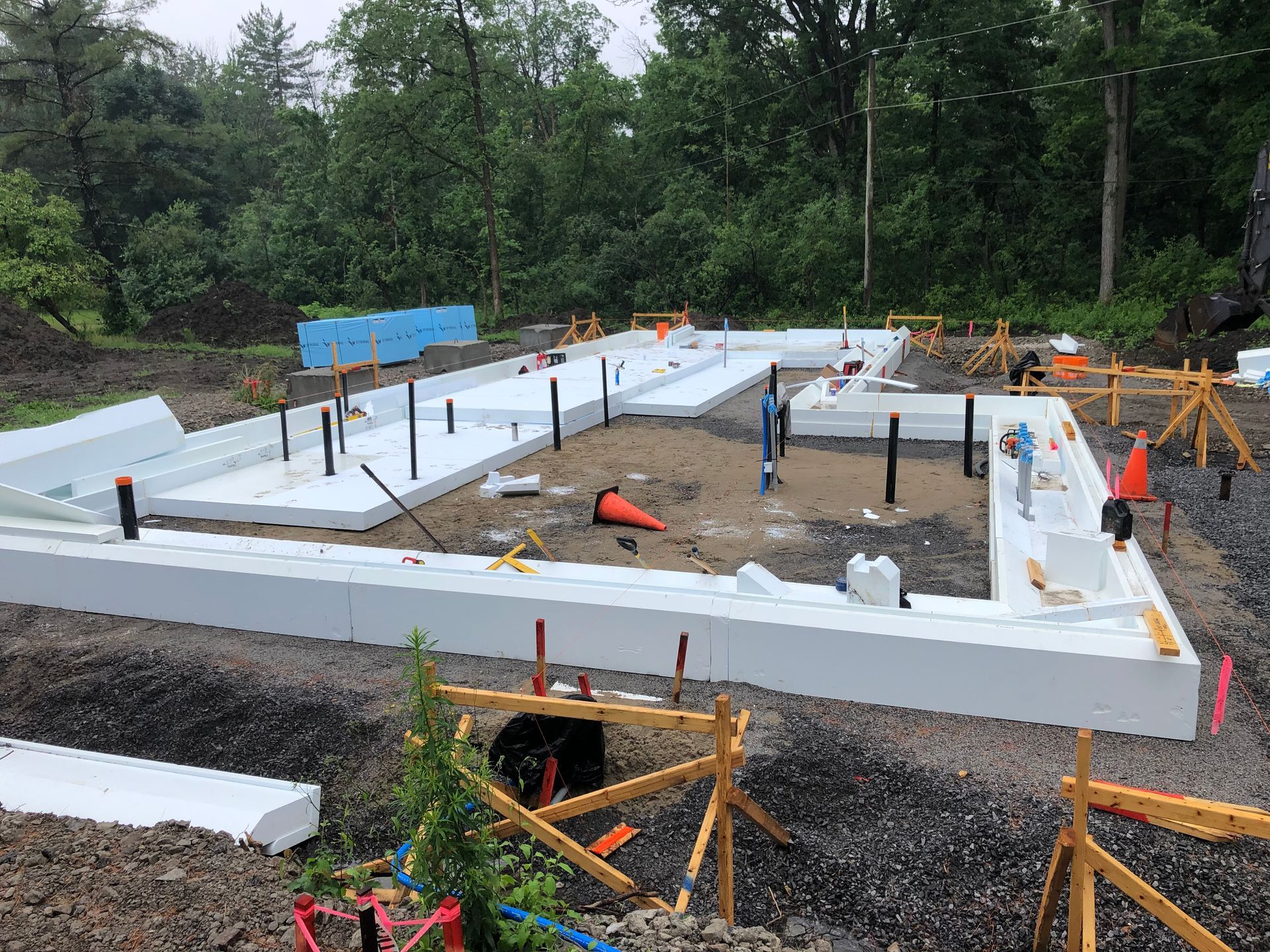 Foundation under construction with white foam forms, black pipes, orange cones, and gravel.