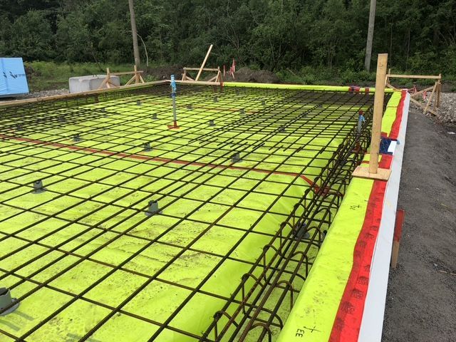 Reinforced concrete foundation under construction; rebar grid on yellow insulation, bordered by wooden forms.