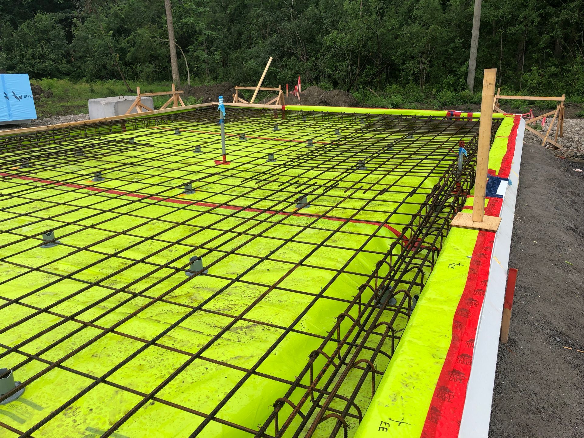 Concrete foundation framework with rebar grid and bright yellow moisture barrier.