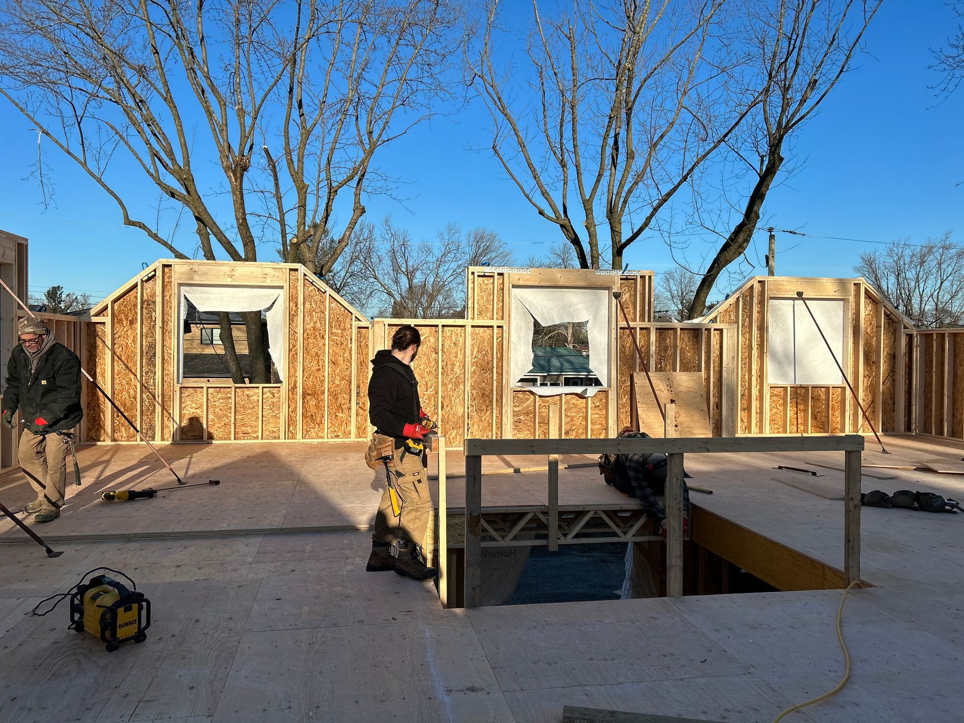Construction workers framing a building with wooden walls and window openings, sunny day.