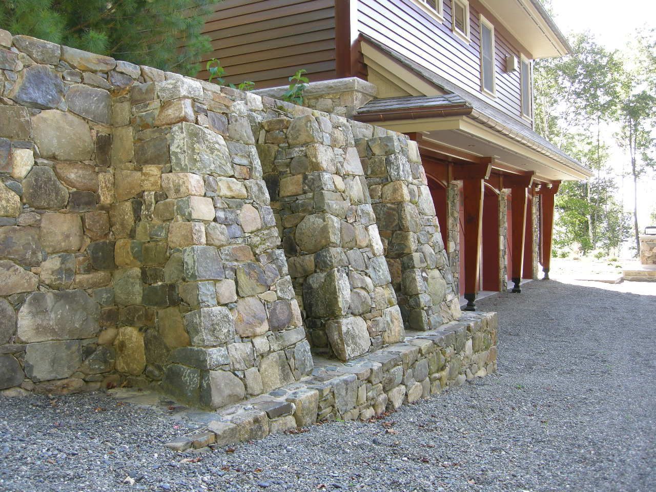 Stone retaining wall with three angled buttresses next to a building with red garage doors.