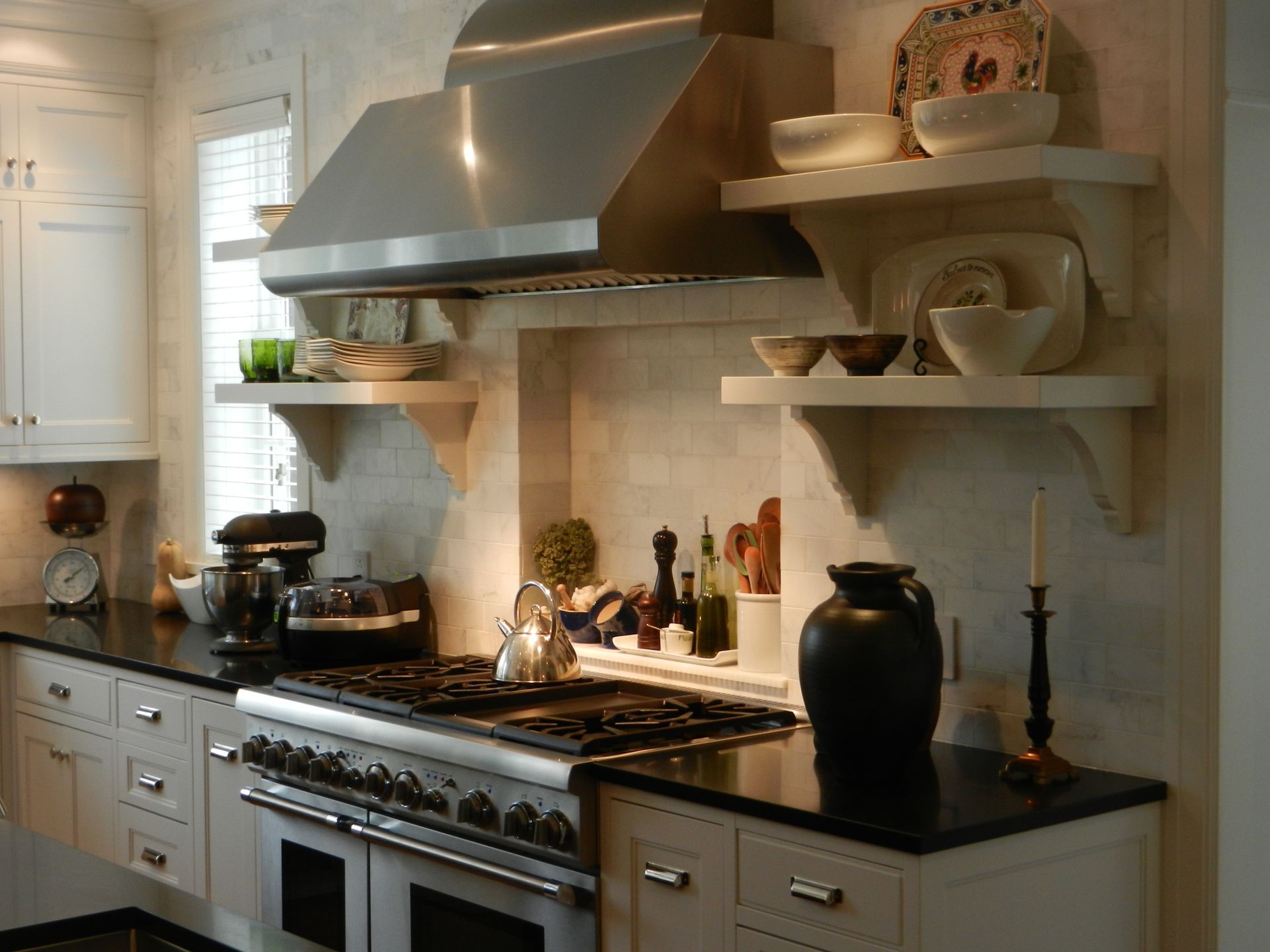 Kitchen with stainless steel range hood, open shelves displaying dishes, and black countertops.