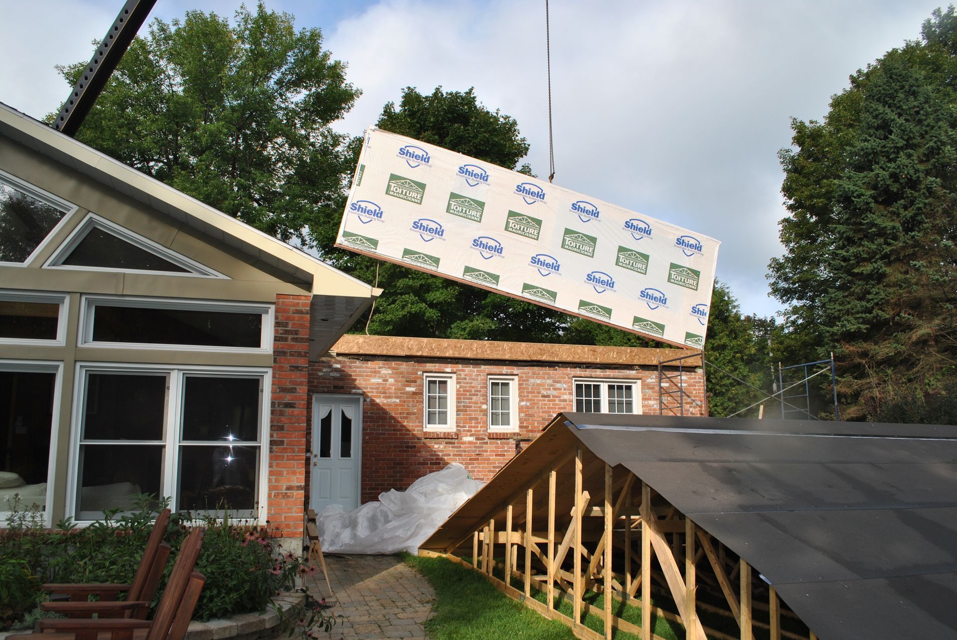 A large construction panel being lifted by a crane towards a building under construction.