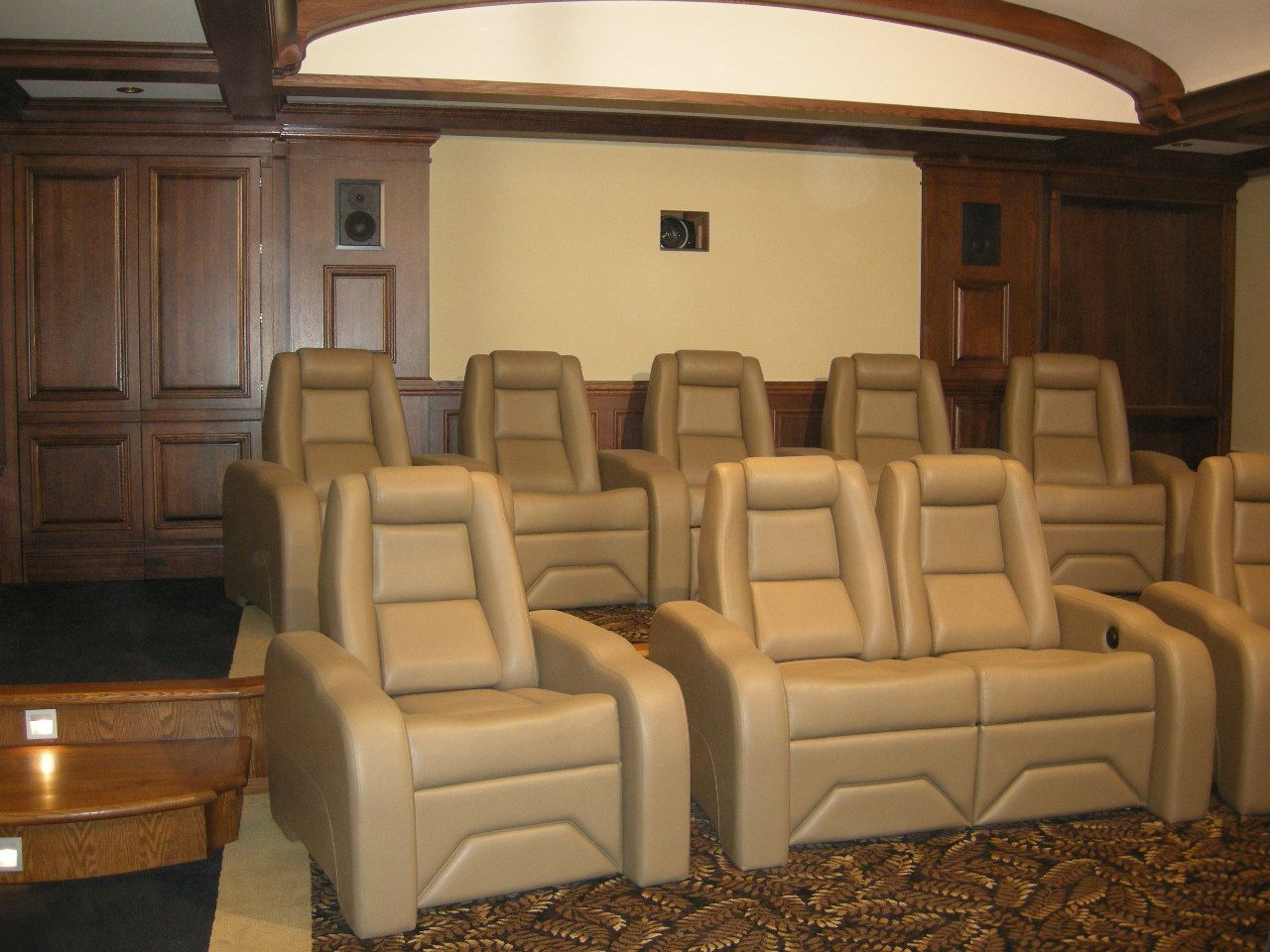 A home theater with tan leather recliners and wood paneling on the walls.
