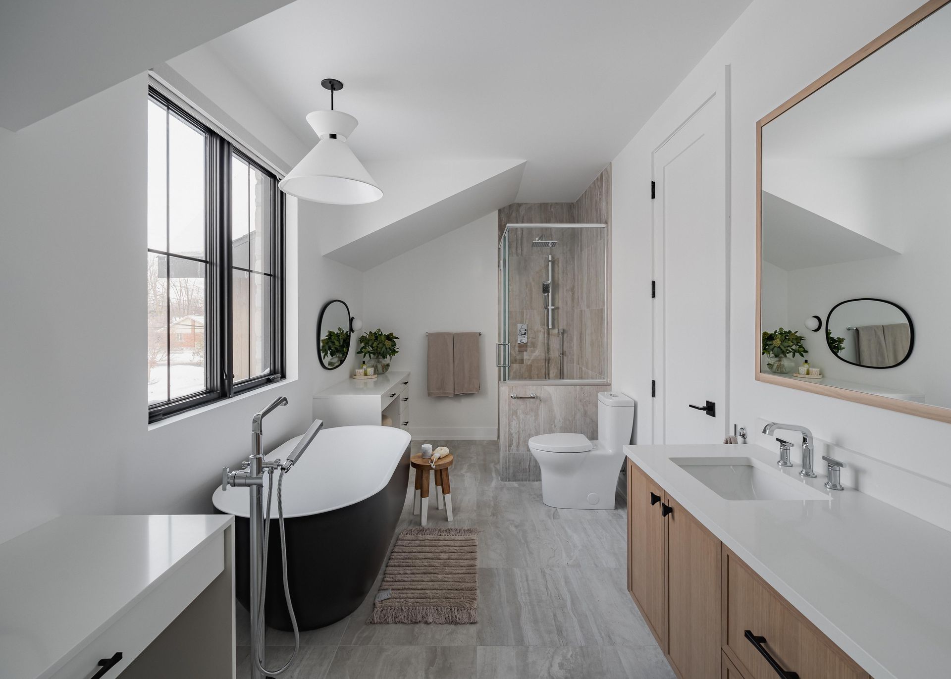 Modern bathroom with black soaking tub, light wood vanity, and a large window.