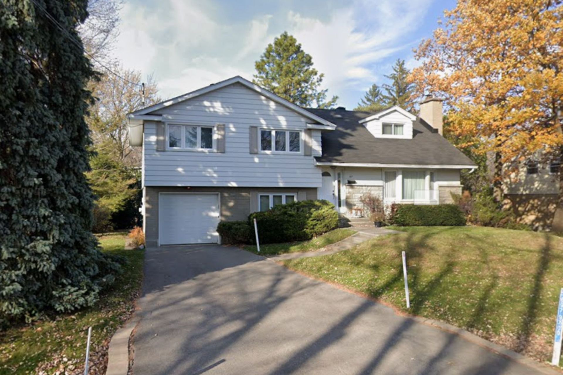 Two-story house with white siding and gray roof, driveway, and landscaping in autumn.