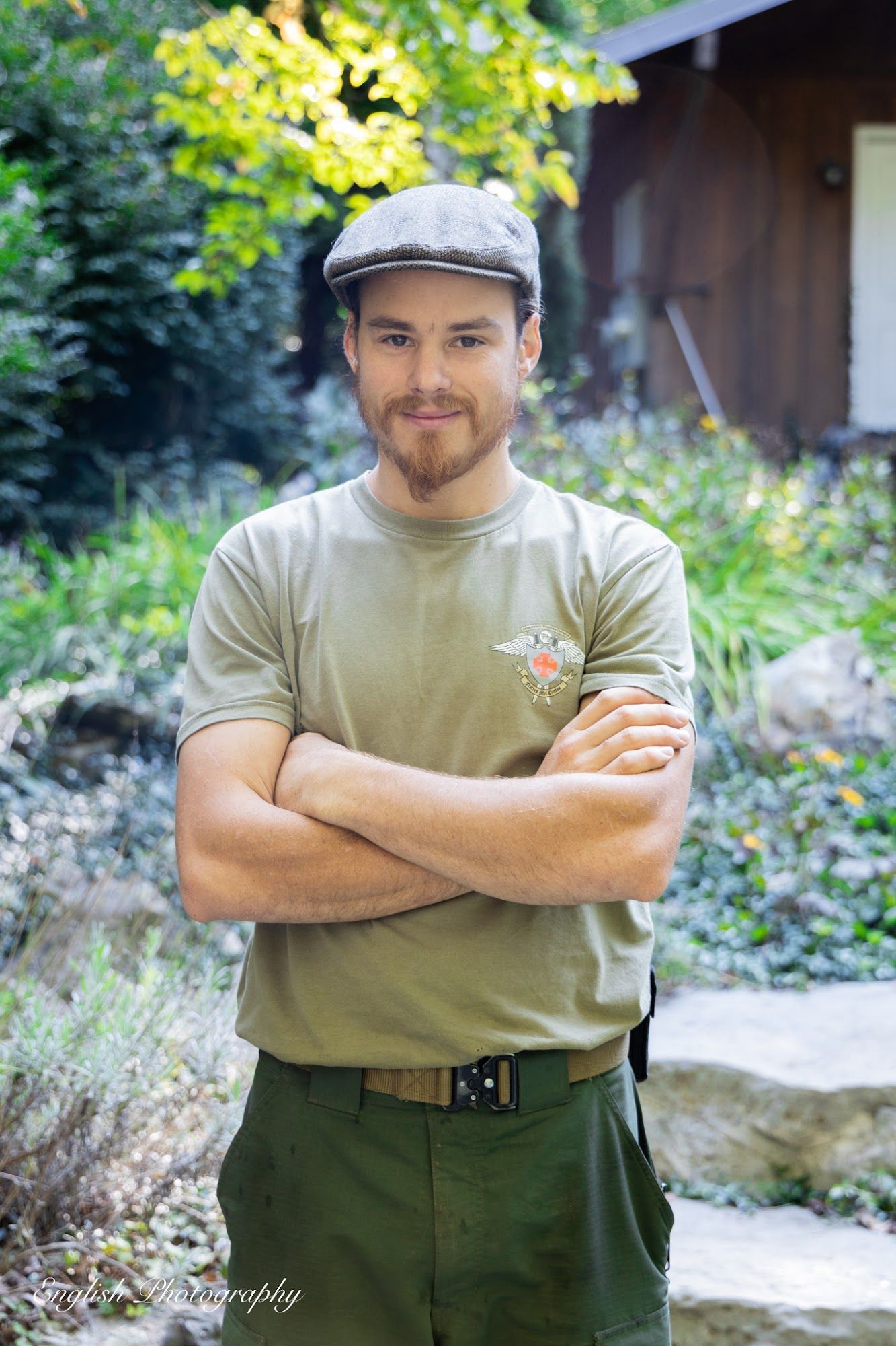 A man wearing a hat and a green shirt is standing with his arms crossed.