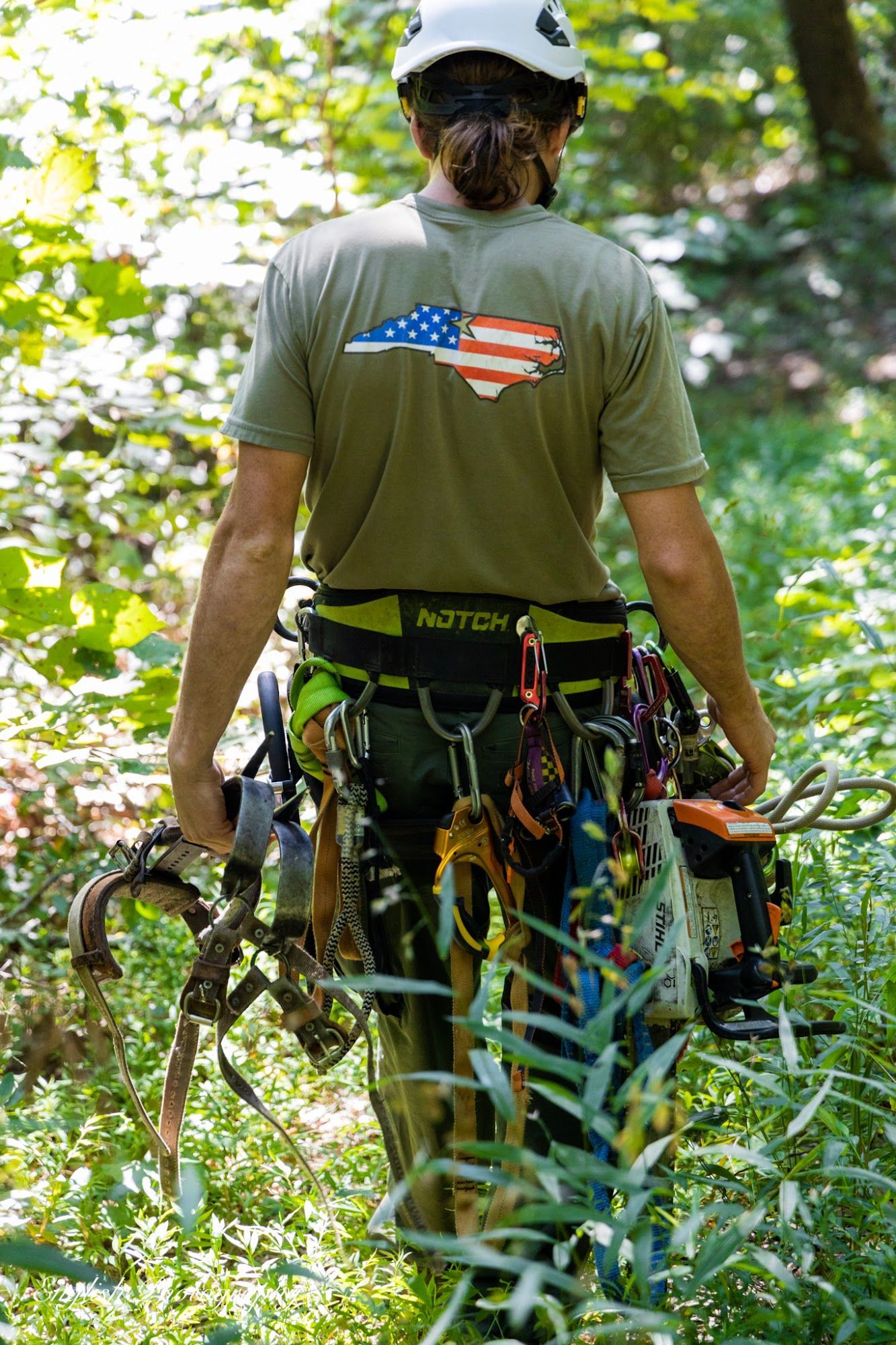 A man is carrying a bunch of climbing gear in the woods.
