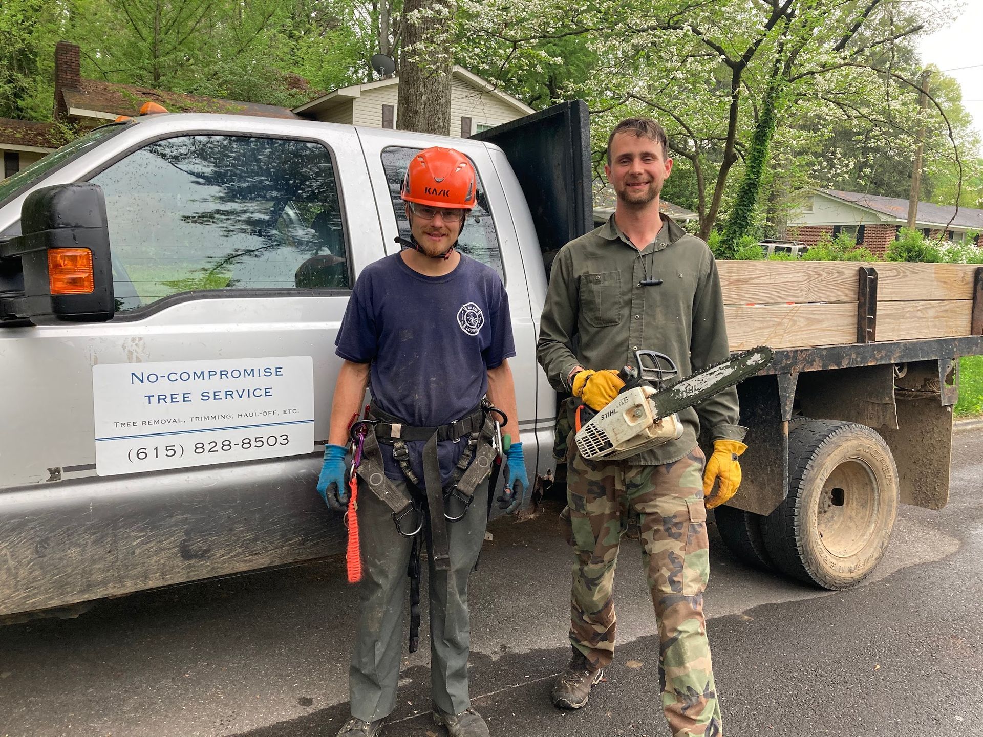 Two men are standing in front of a truck with a chainsaw.