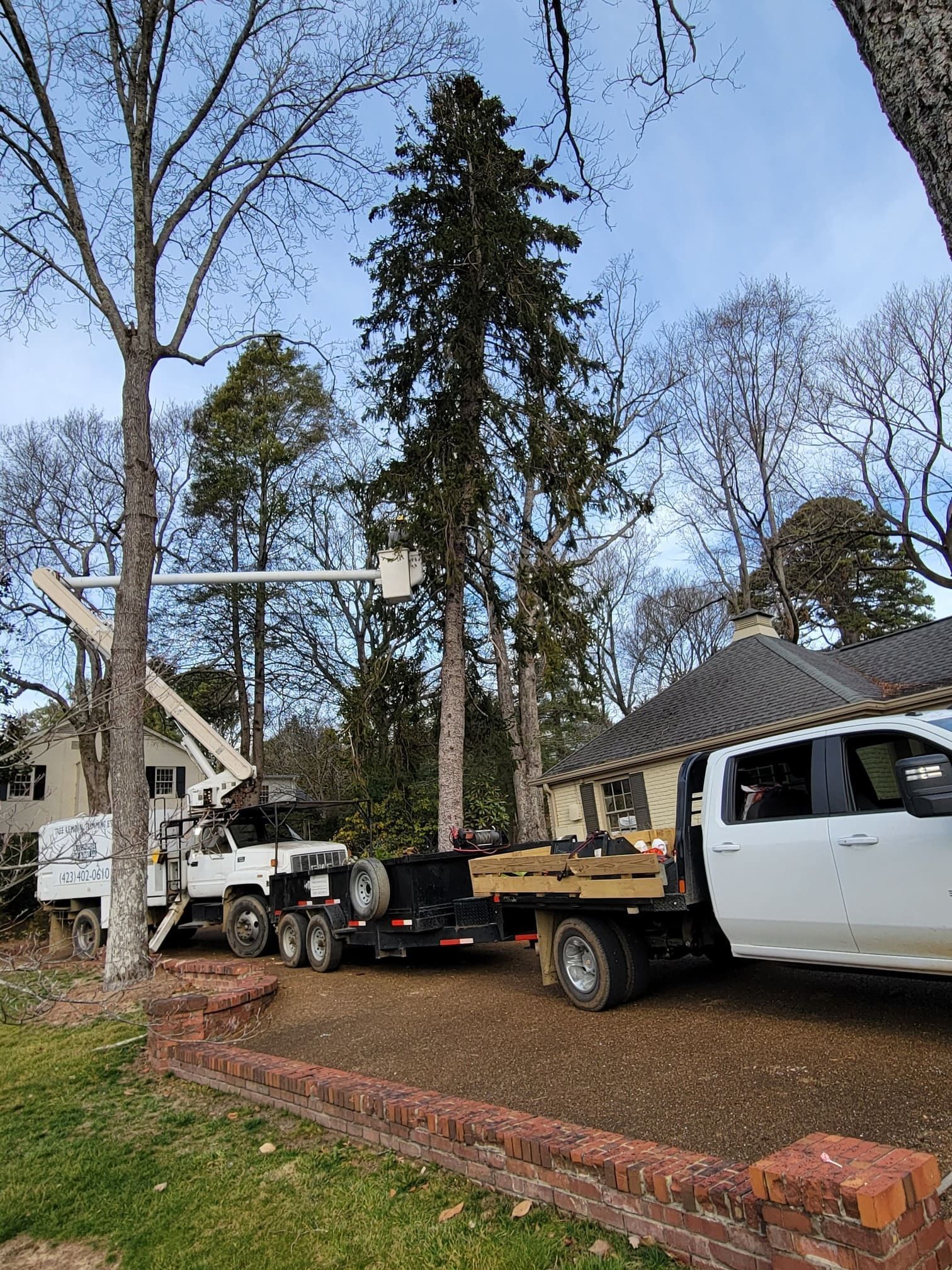 A white truck is parked in front of a house with a crane on the back of it.