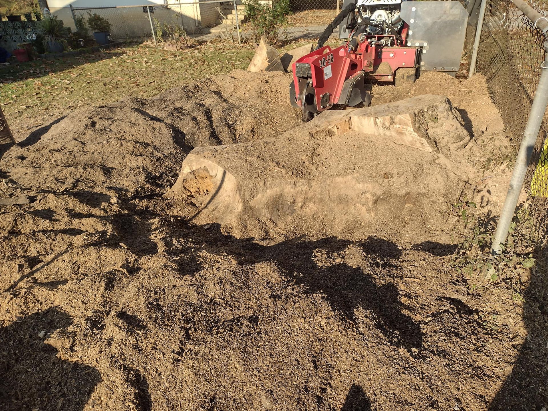 A red tractor is working on a pile of dirt in a yard.