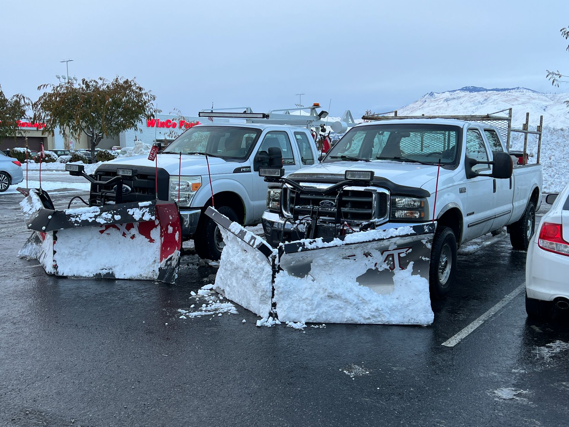 Two snow plows are parked next to each other in a parking lot.