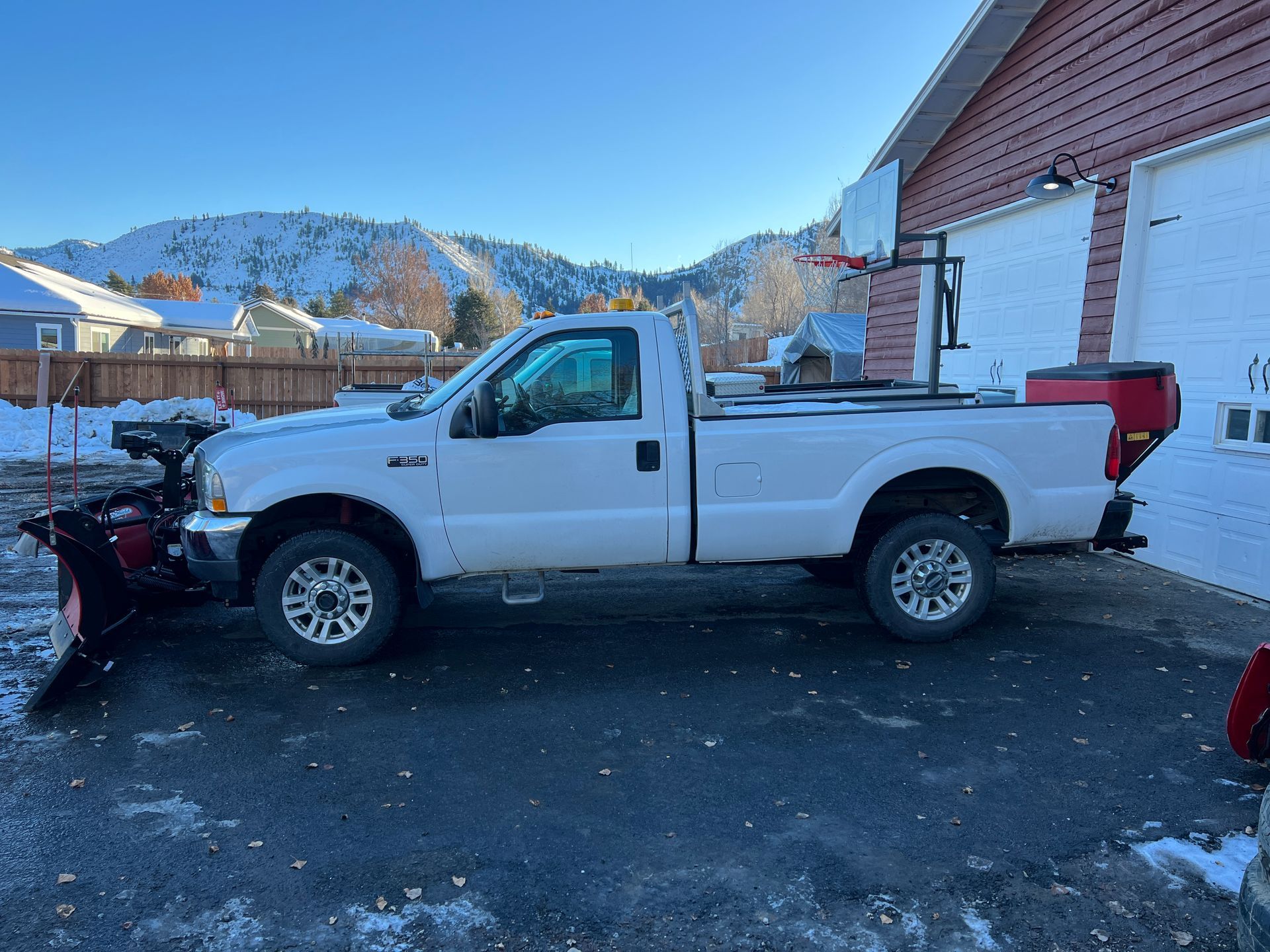 A white truck with a snow plow attached to it is parked in front of a house.