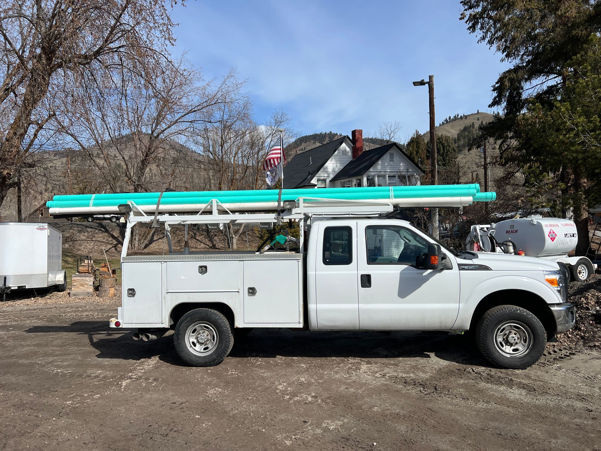 A white truck with a green pipe on top of it is parked in front of a house.