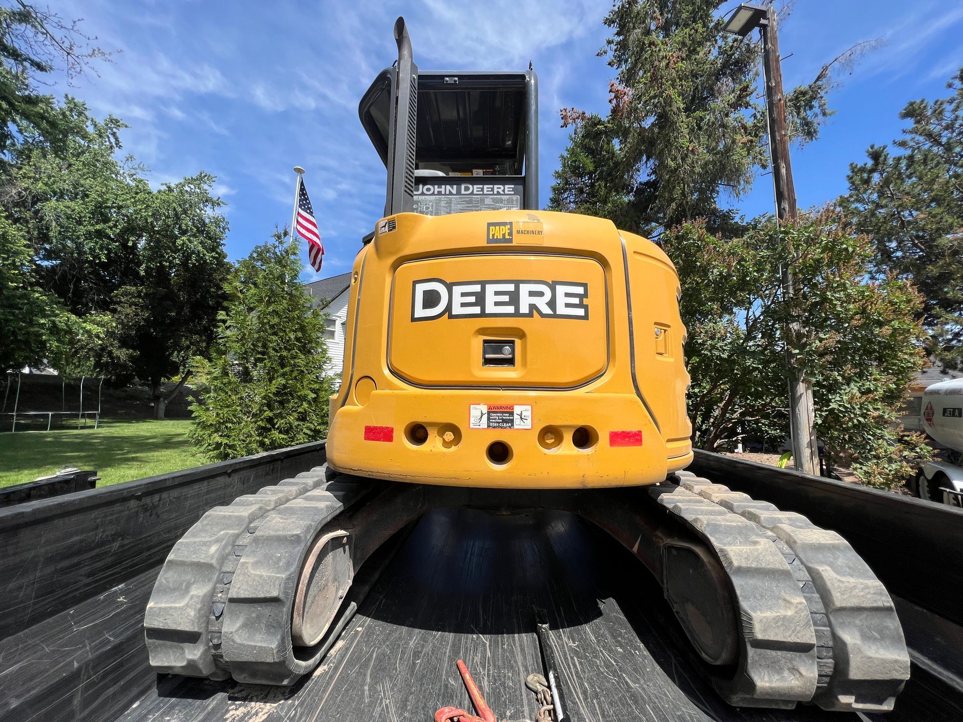 A yellow deere excavator is sitting in the back of a truck.