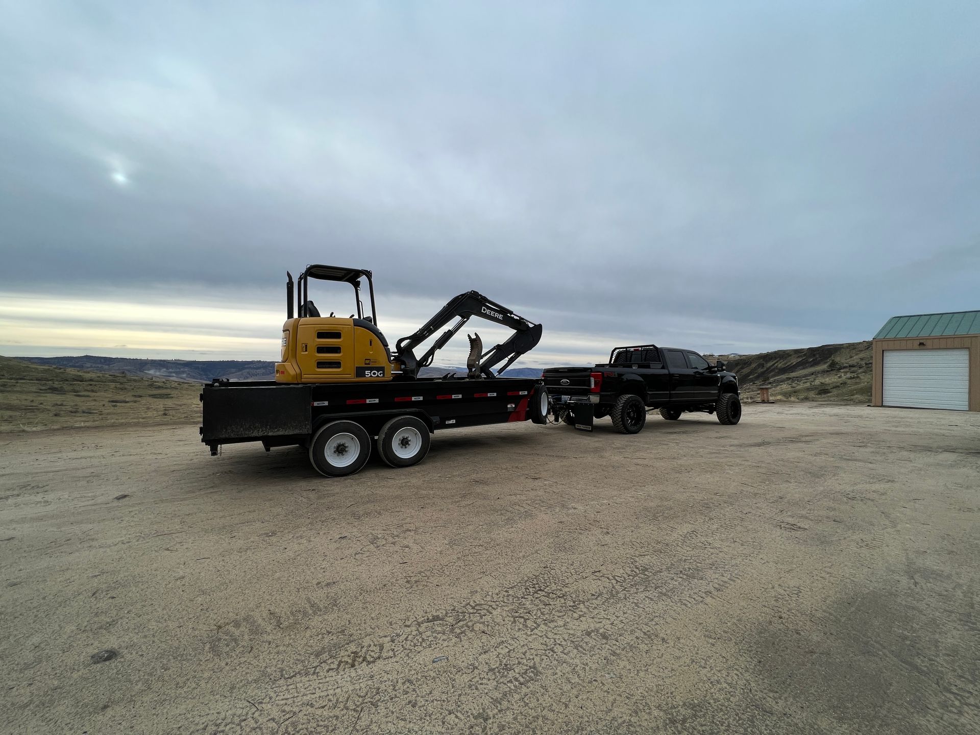 A black truck is towing a yellow excavator on a flatbed trailer