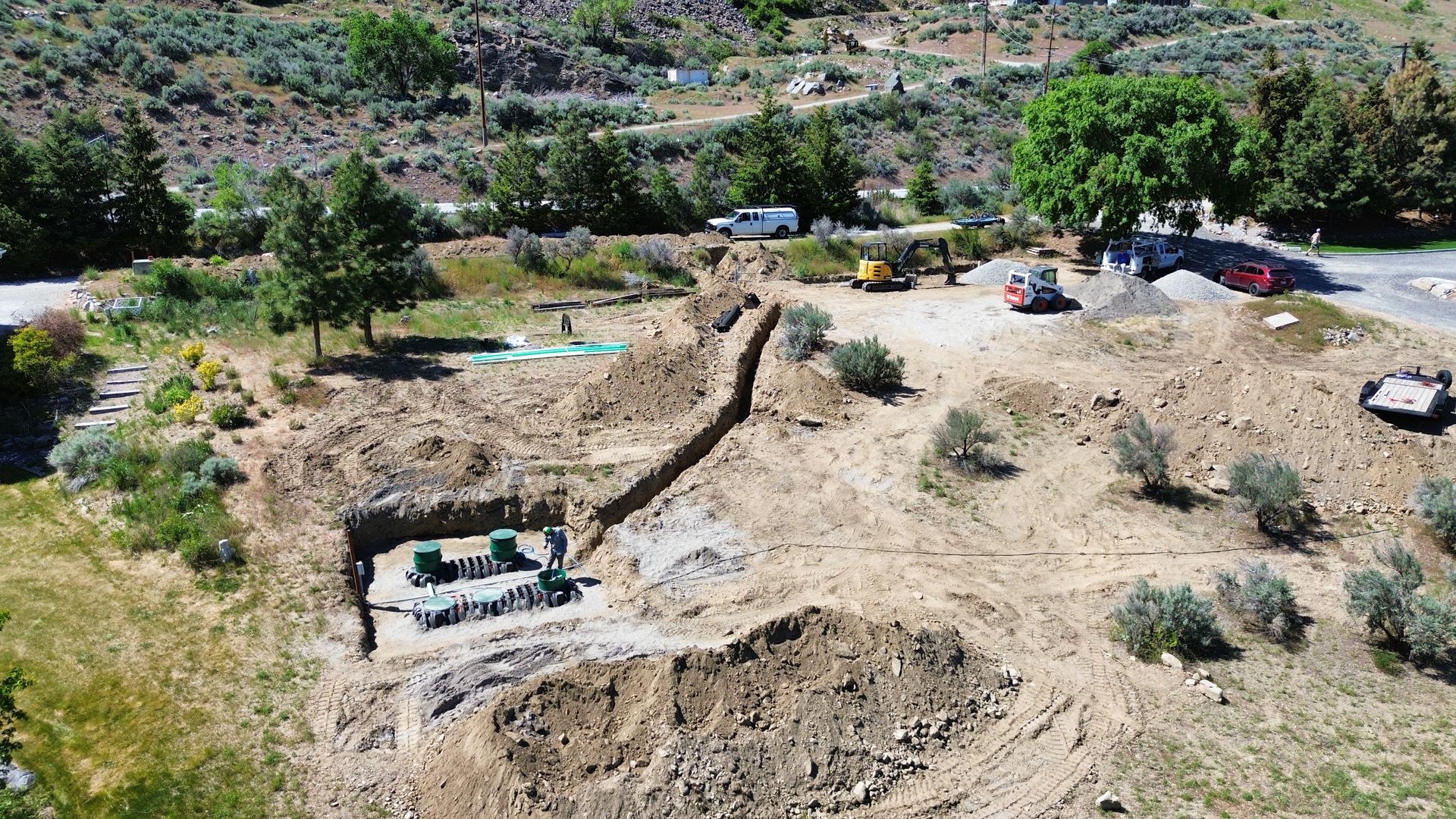 An aerial view of a dirt field with trees and a road in the background.
