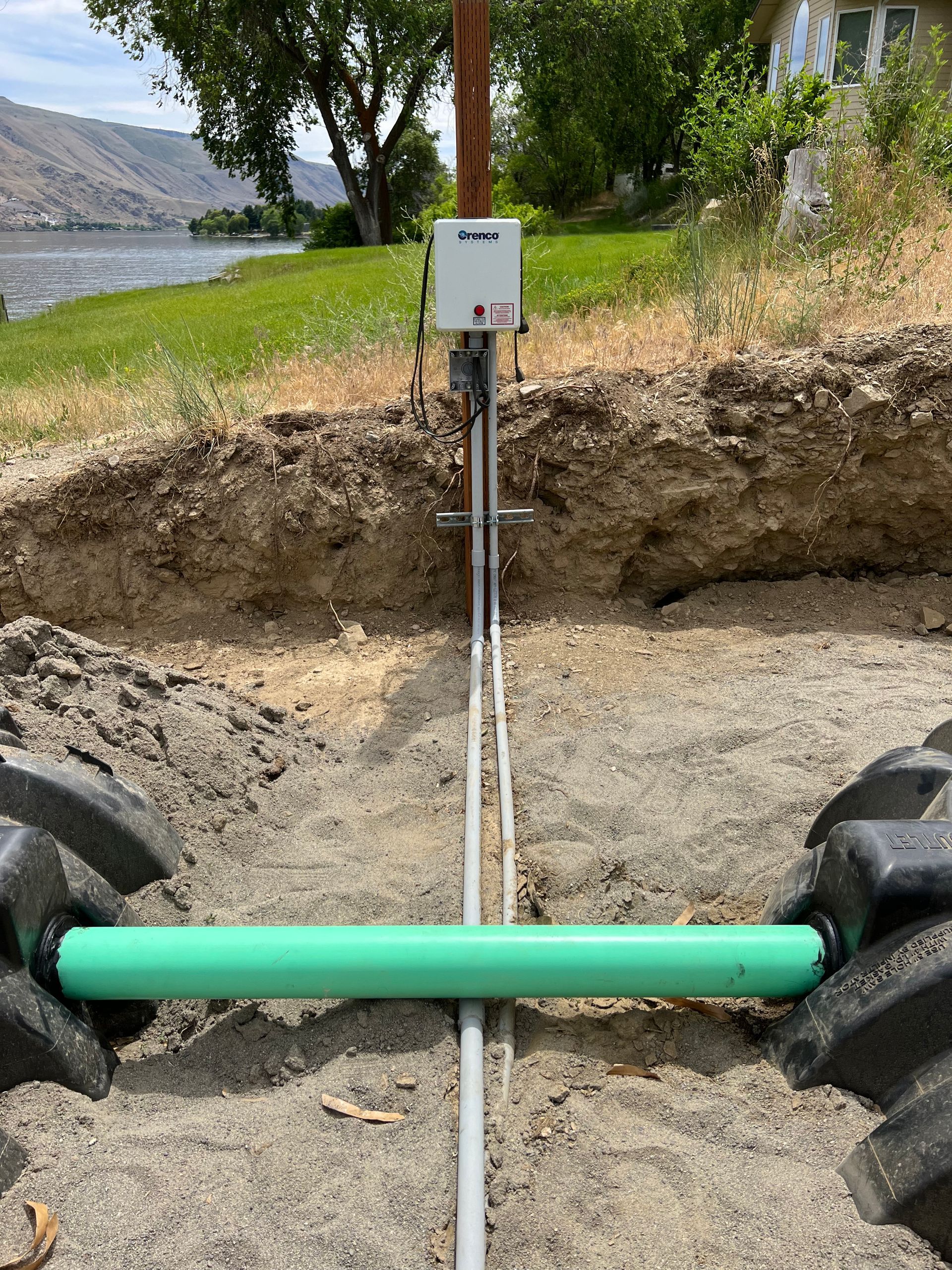A green pipe is sitting in the dirt next to a tractor tire.