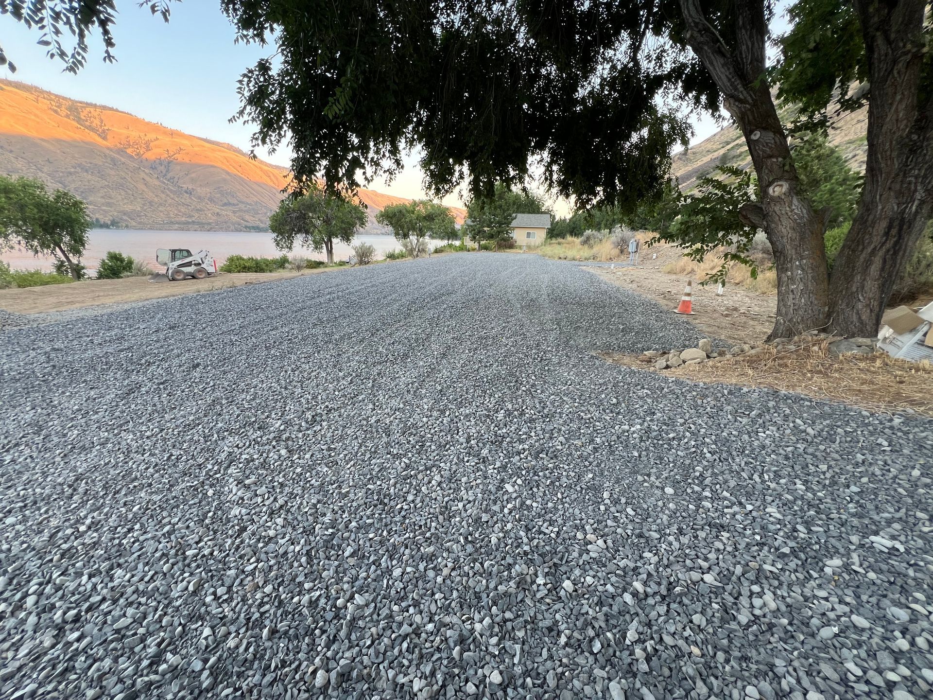 A gravel road with a tree in the background and a lake in the background.