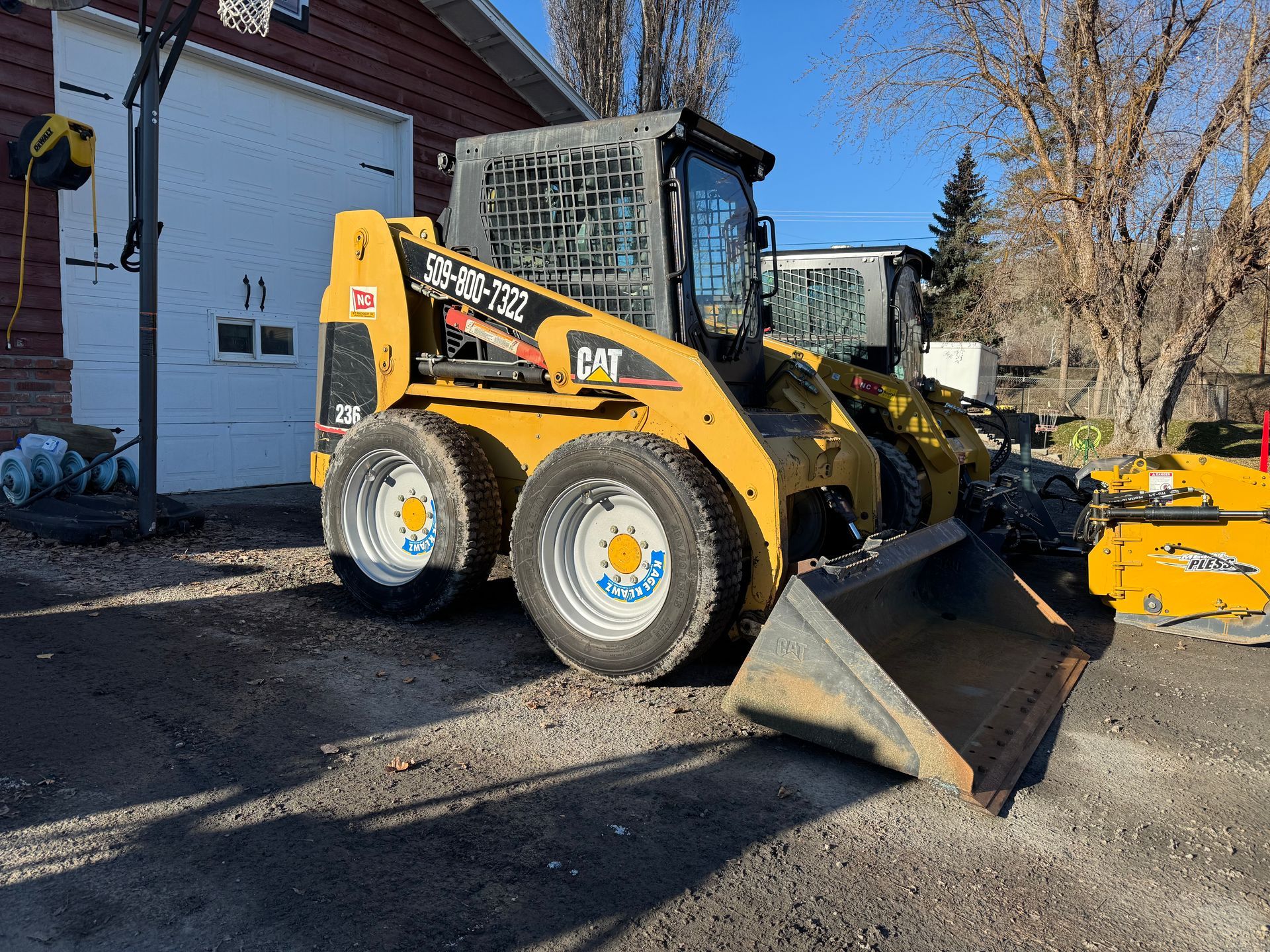 A yellow cat skid steer loader is parked in front of a garage.