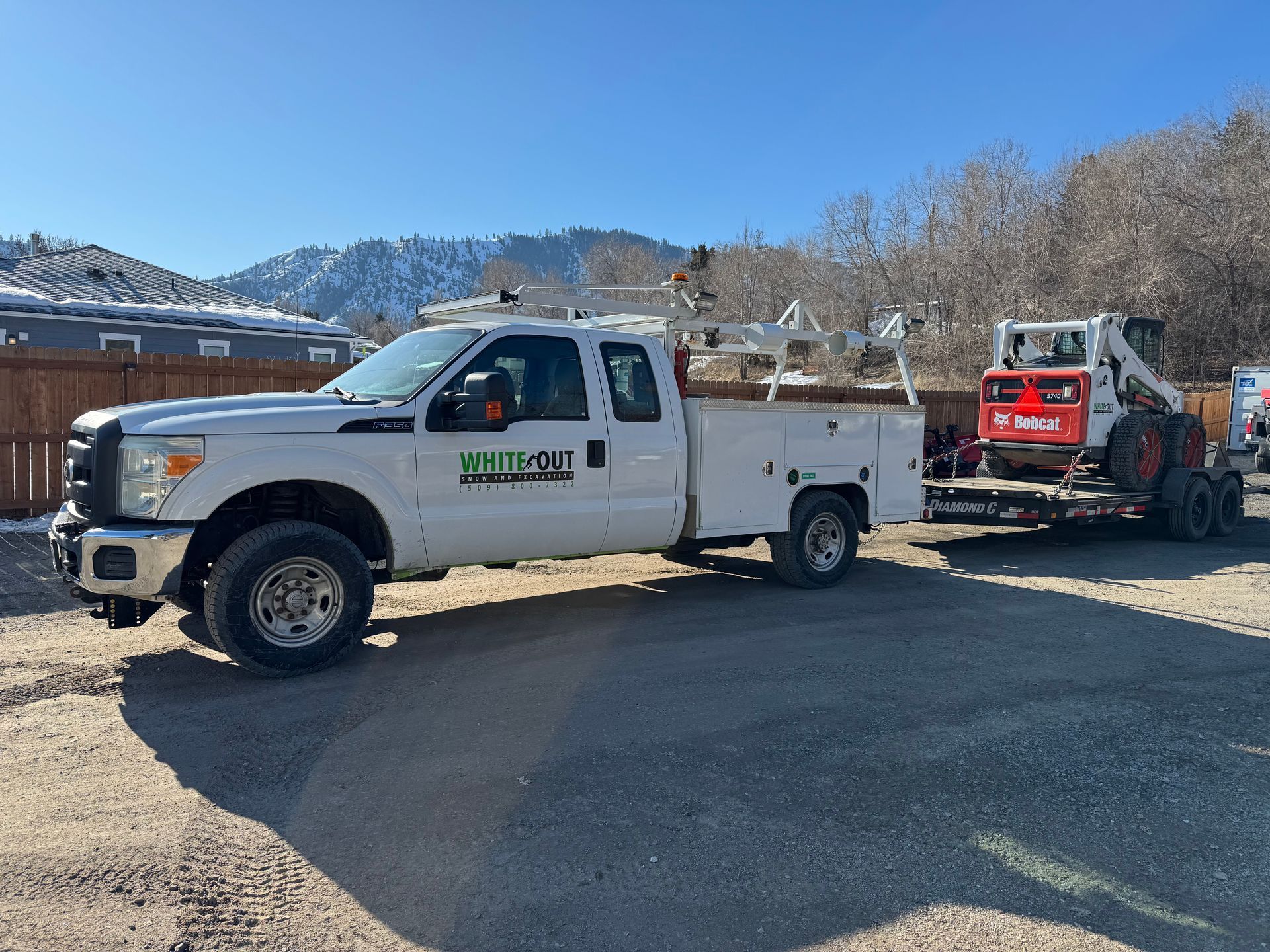 A white truck is towing a small excavator on a trailer.