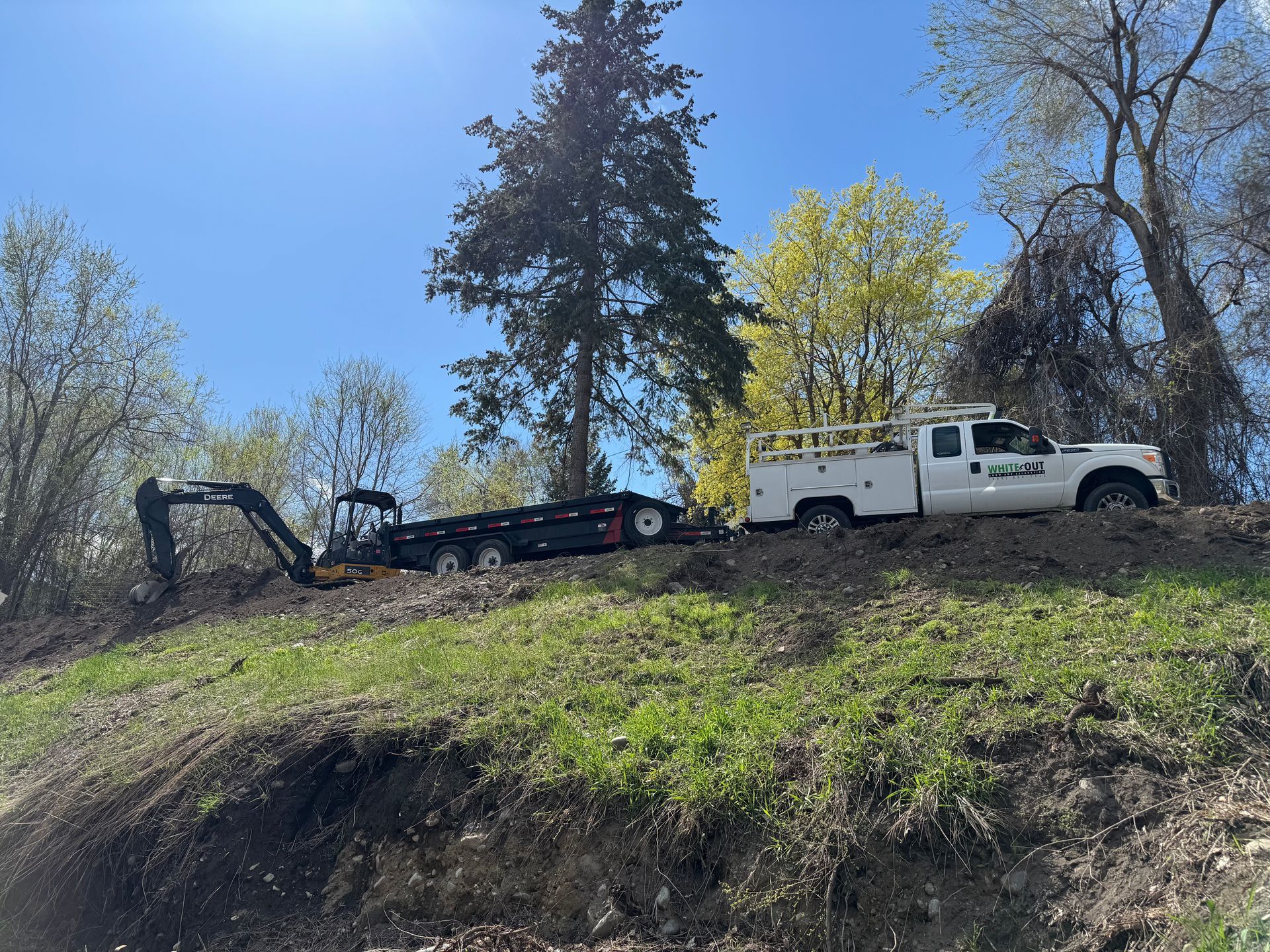 A white truck with a trailer attached to it is parked on a hill.