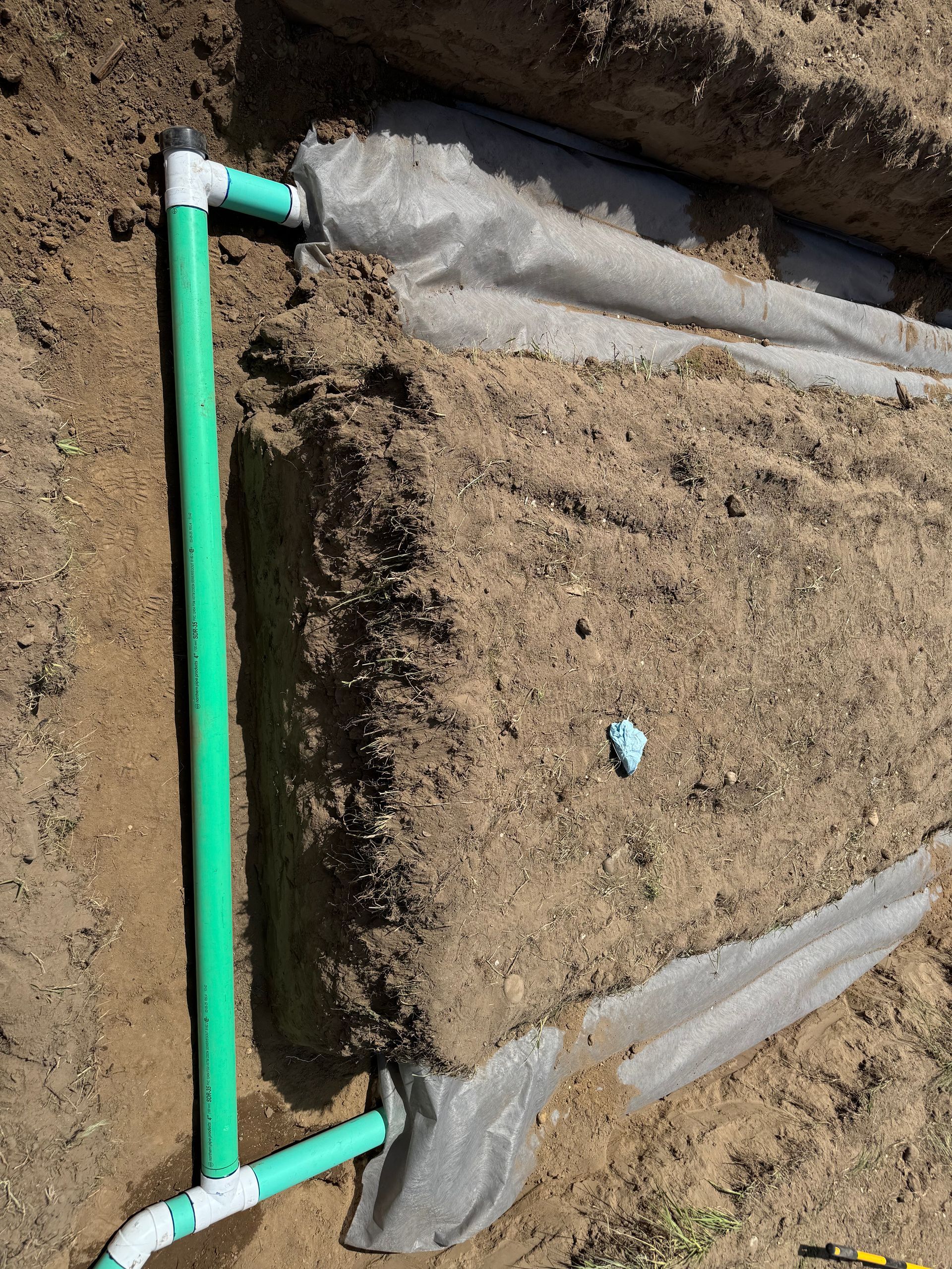 A green pipe is laying in the dirt next to a piece of plastic.