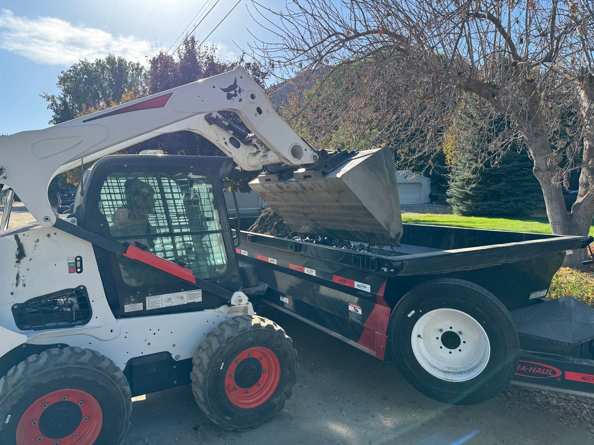A bobcat is parked on the side of the road next to a dump truck.