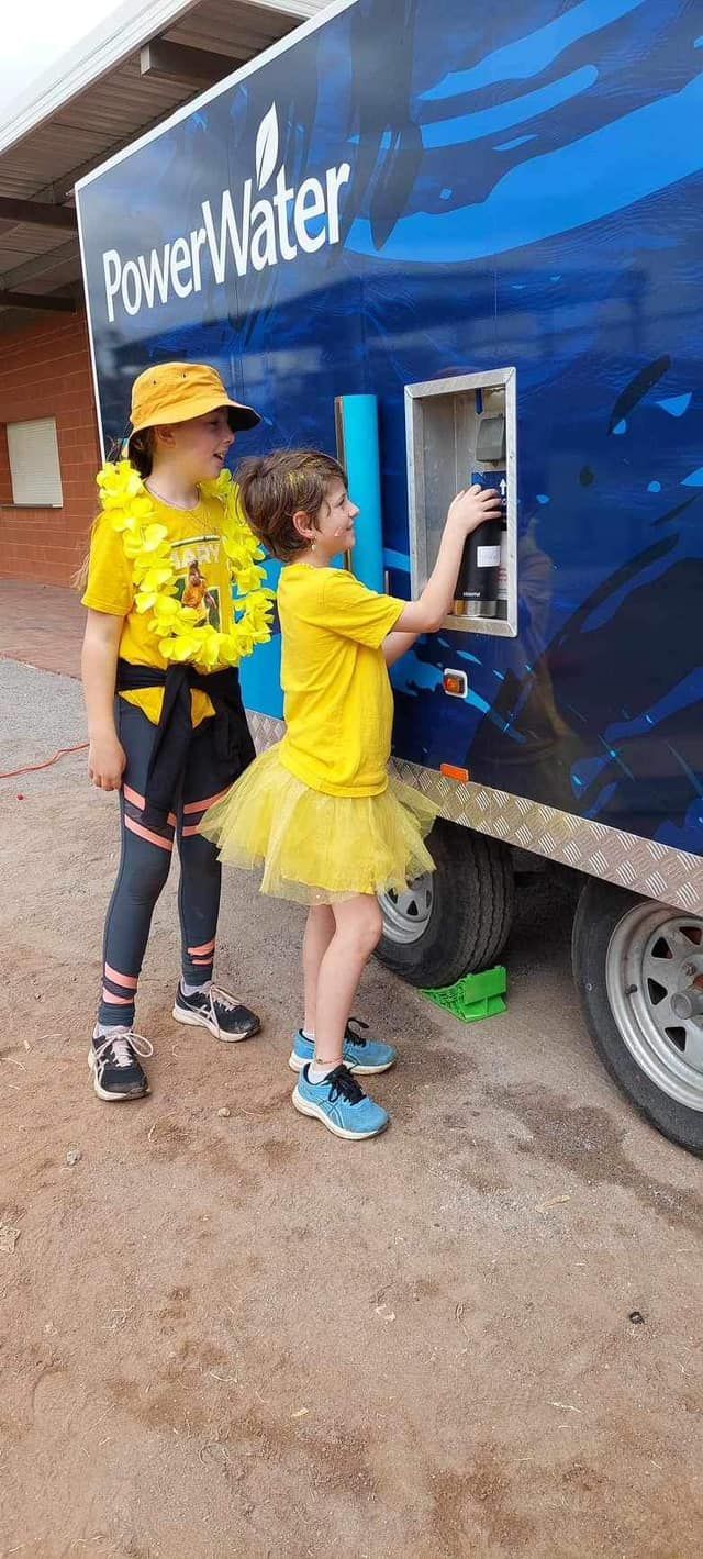 Two children in yellow outfits filling a bottle from a 