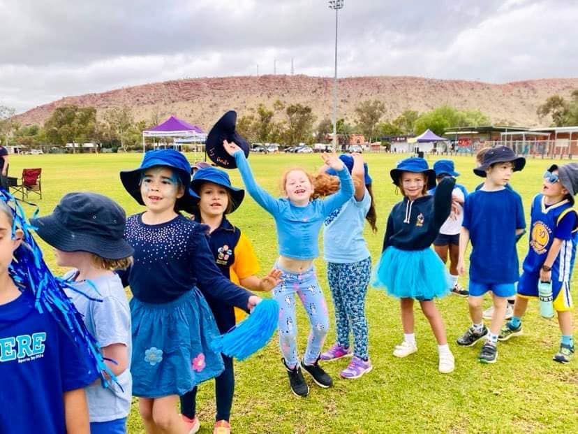 Children in blue outfits pose and celebrate at a park, with a red rock formation in the background.