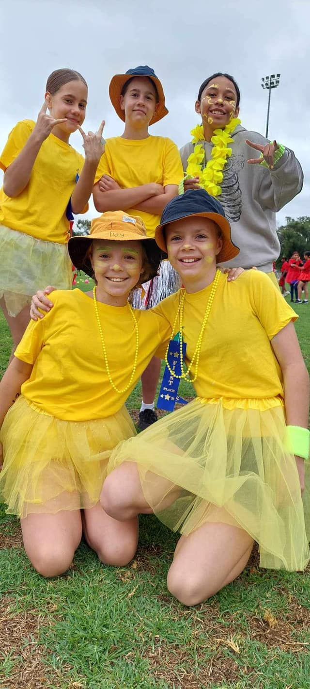 Group of children wearing yellow outfits, hats, posing on grass field.